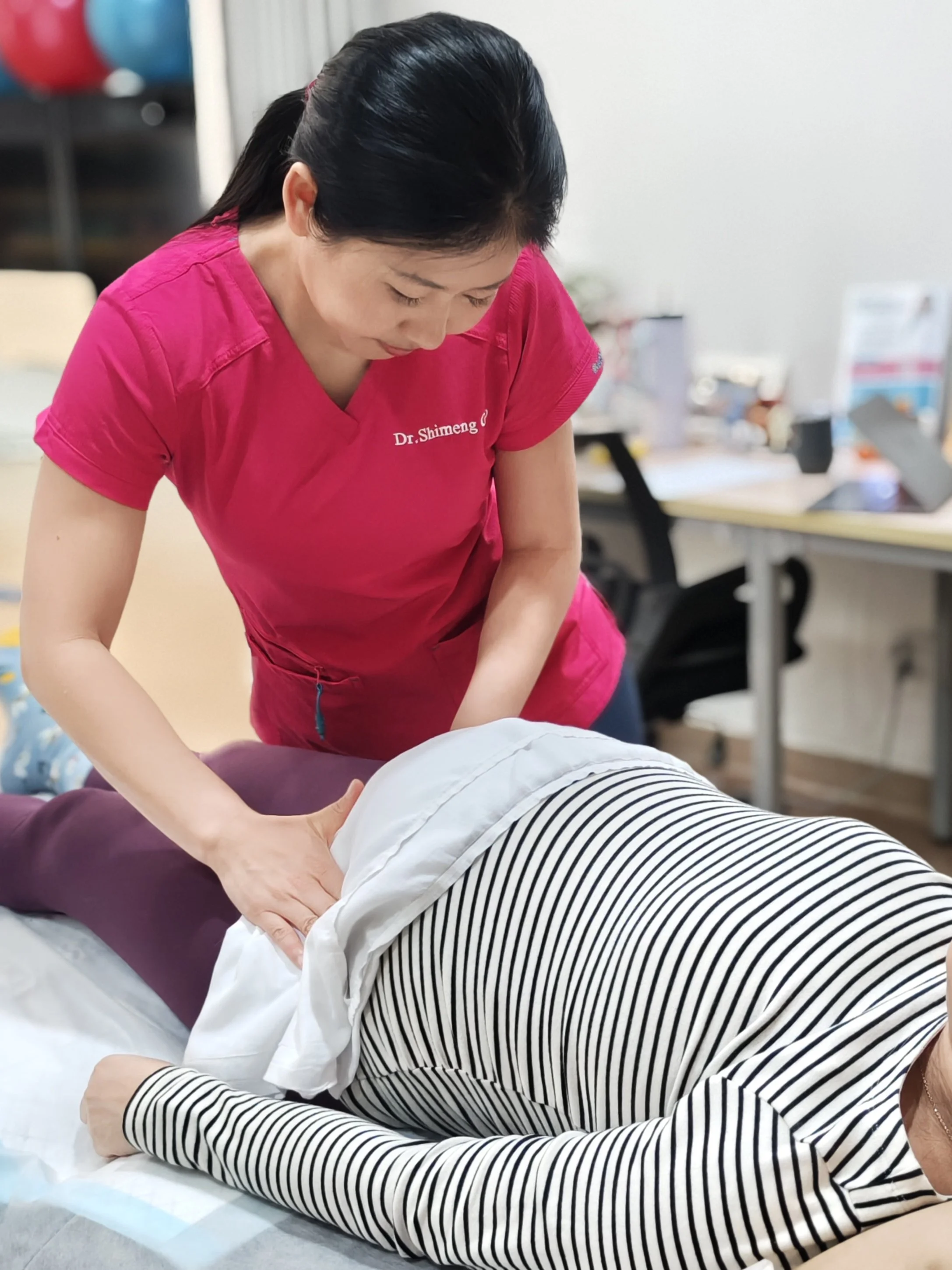 A healthcare professional, wearing a pink uniform, administering chiropractic care to a patient lying face down on a treatment table.