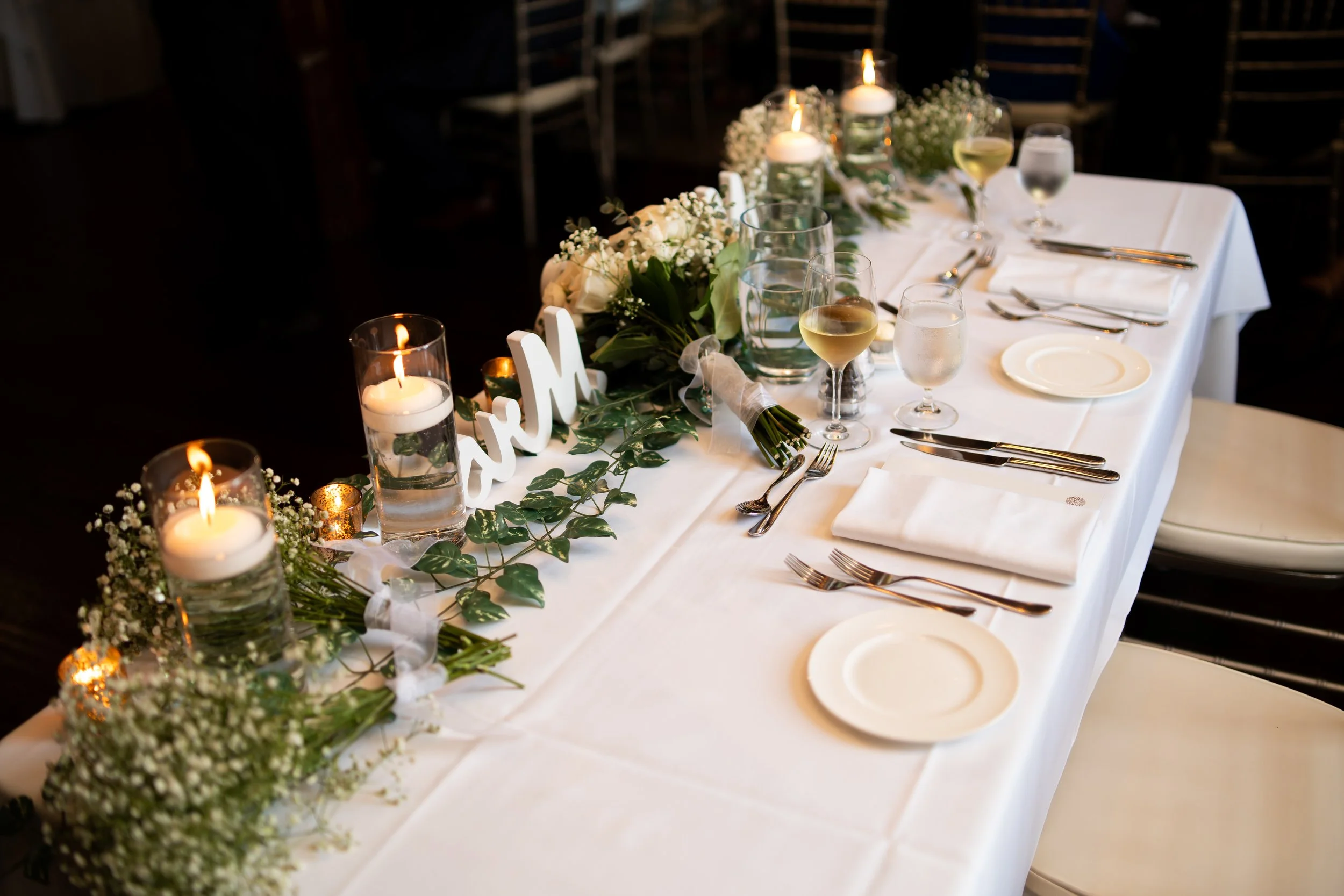 Wedding reception table decorated with candles, white flowers, greenery, and 