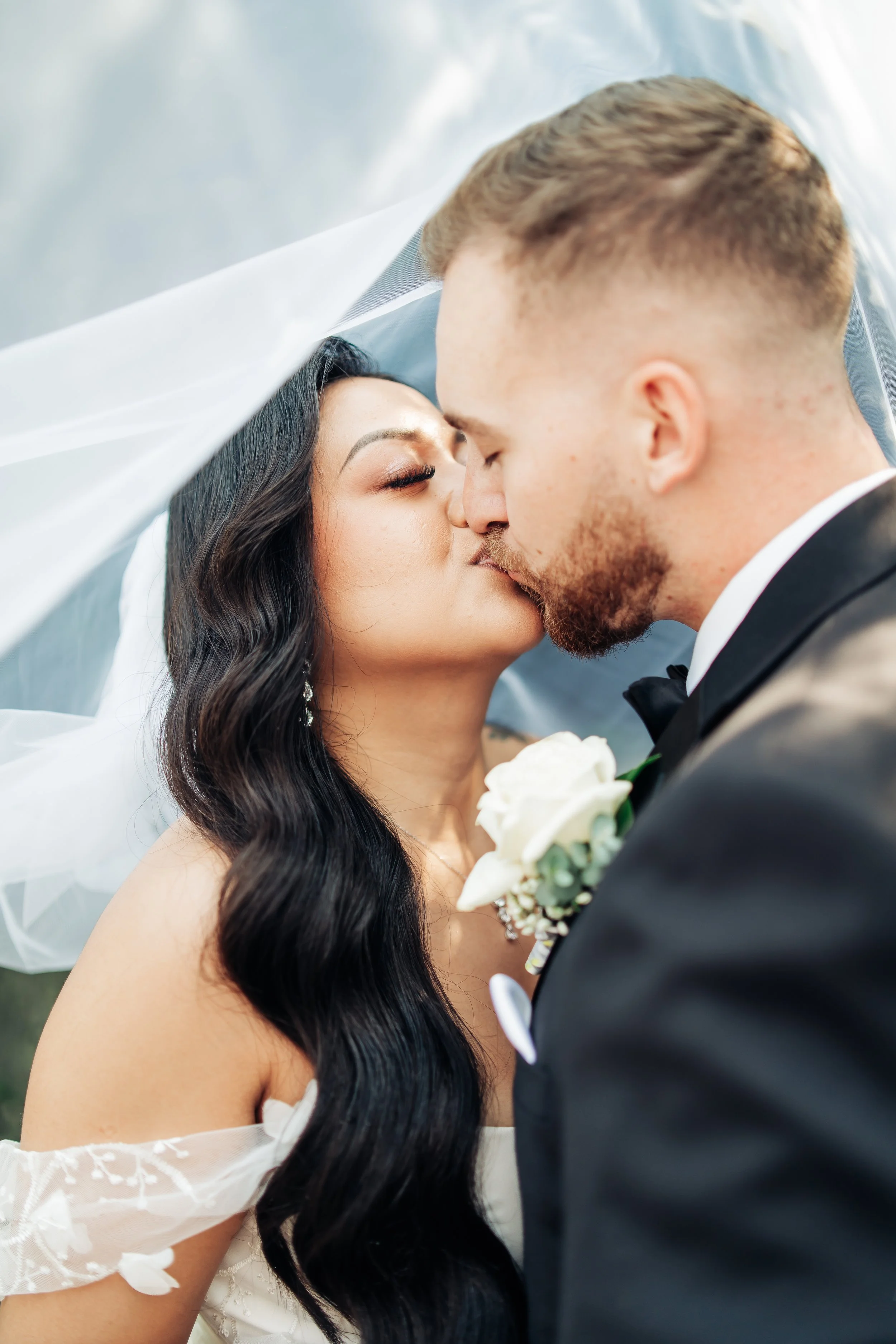 A bride and groom kissing under a white veil during their wedding.