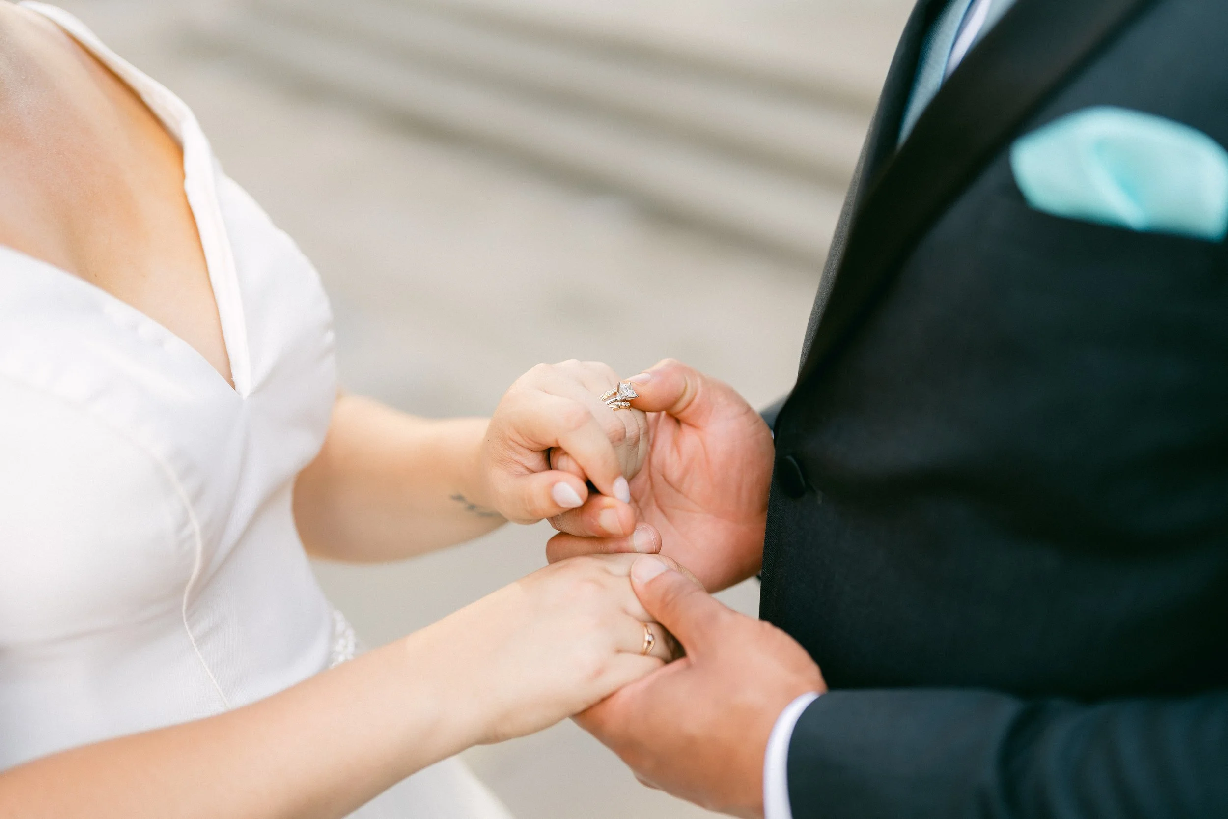 Close-up of a bride and groom holding hands, with the bride placing a wedding ring on the groom's finger during their wedding ceremony.