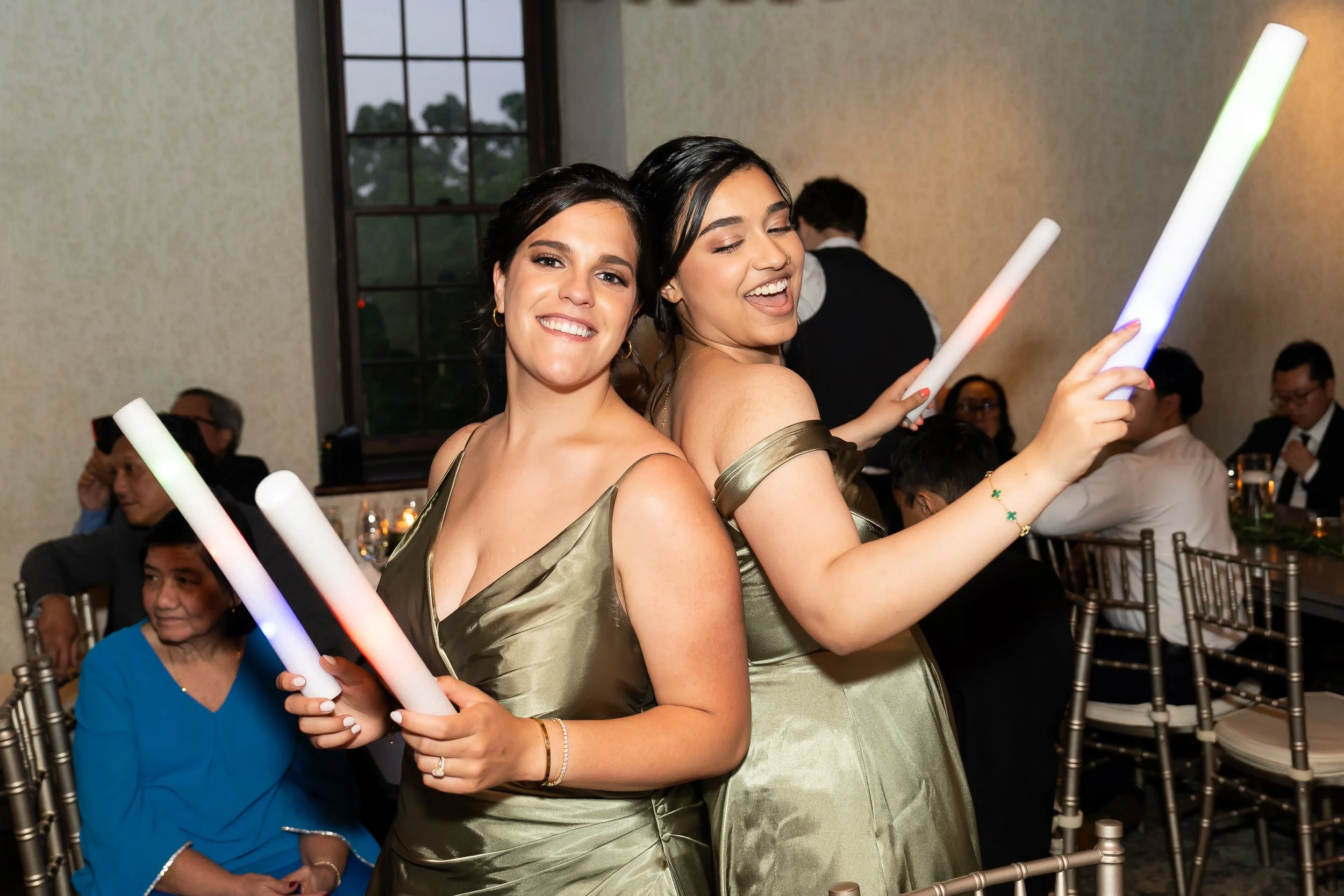 Two women in gold dresses dancing with glow sticks at a celebration event.