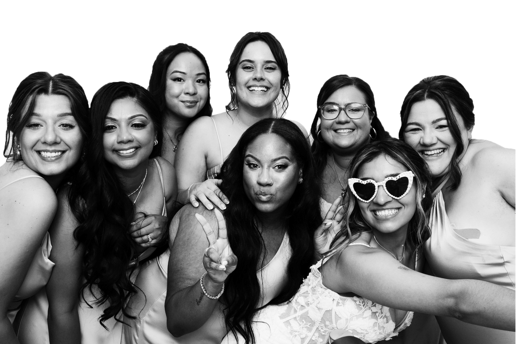Group of nine smiling women taking a selfie together, one woman wearing heart-shaped sunglasses, in black and white