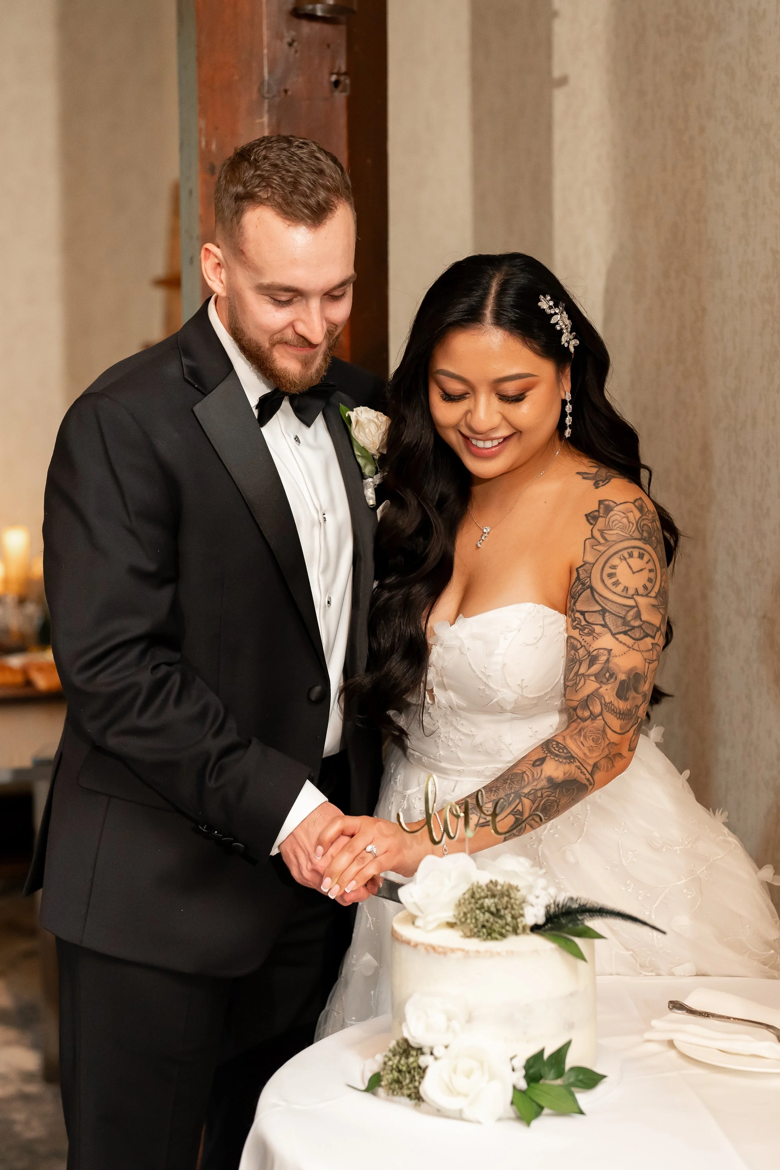 A newly married couple, in wedding attire, cutting a wedding cake together, smiling.