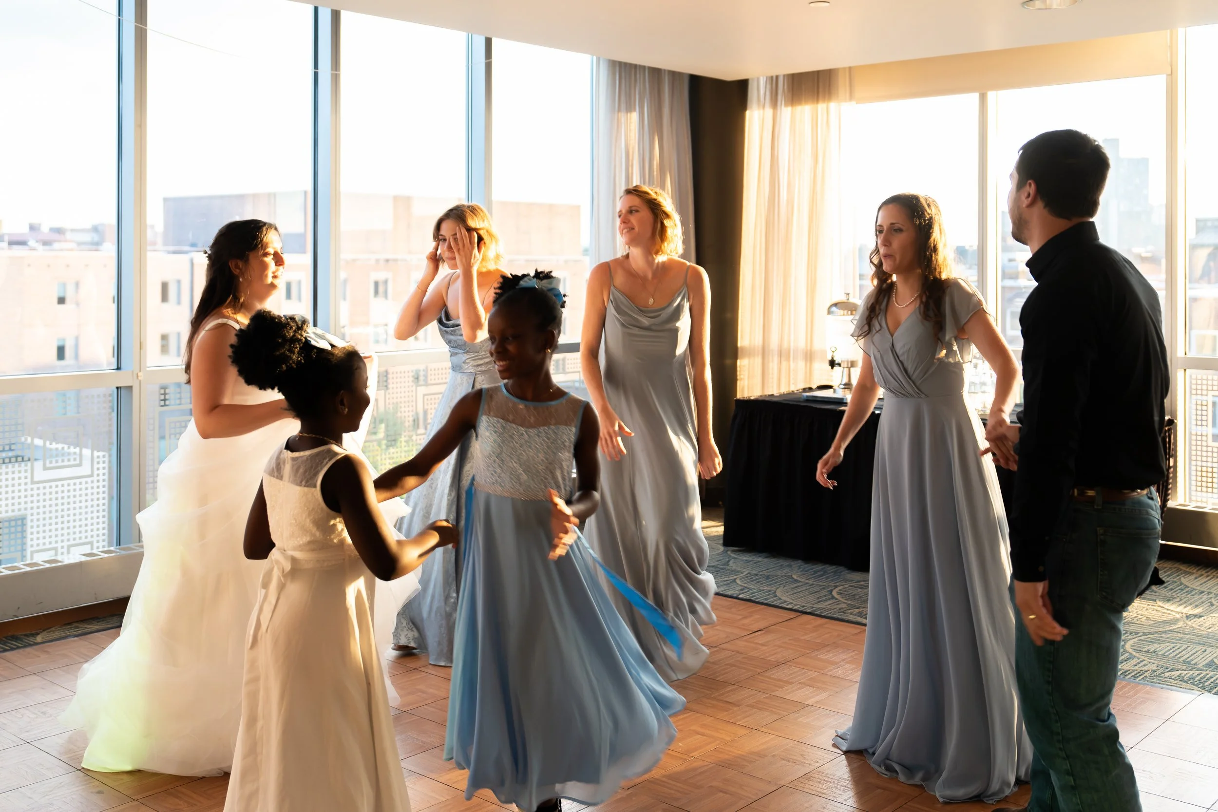 A group of people dancing and socializing in a bright indoor space with large windows and city view.
