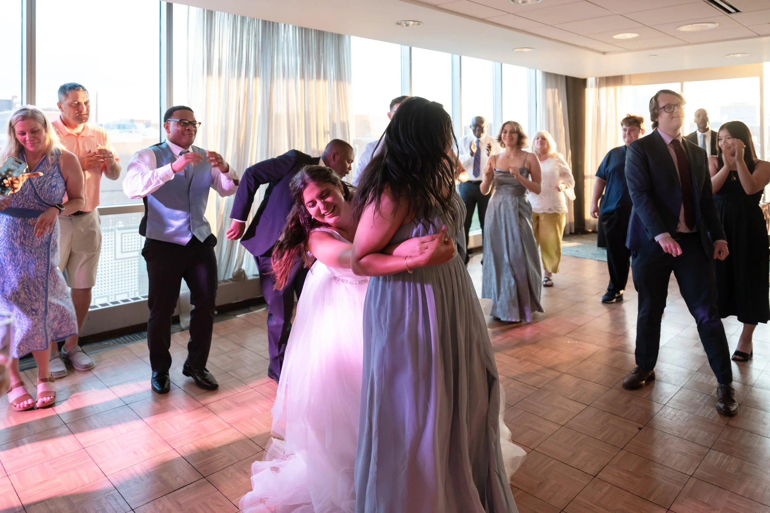 People dancing at a wedding reception in a brightly lit room with large windows.