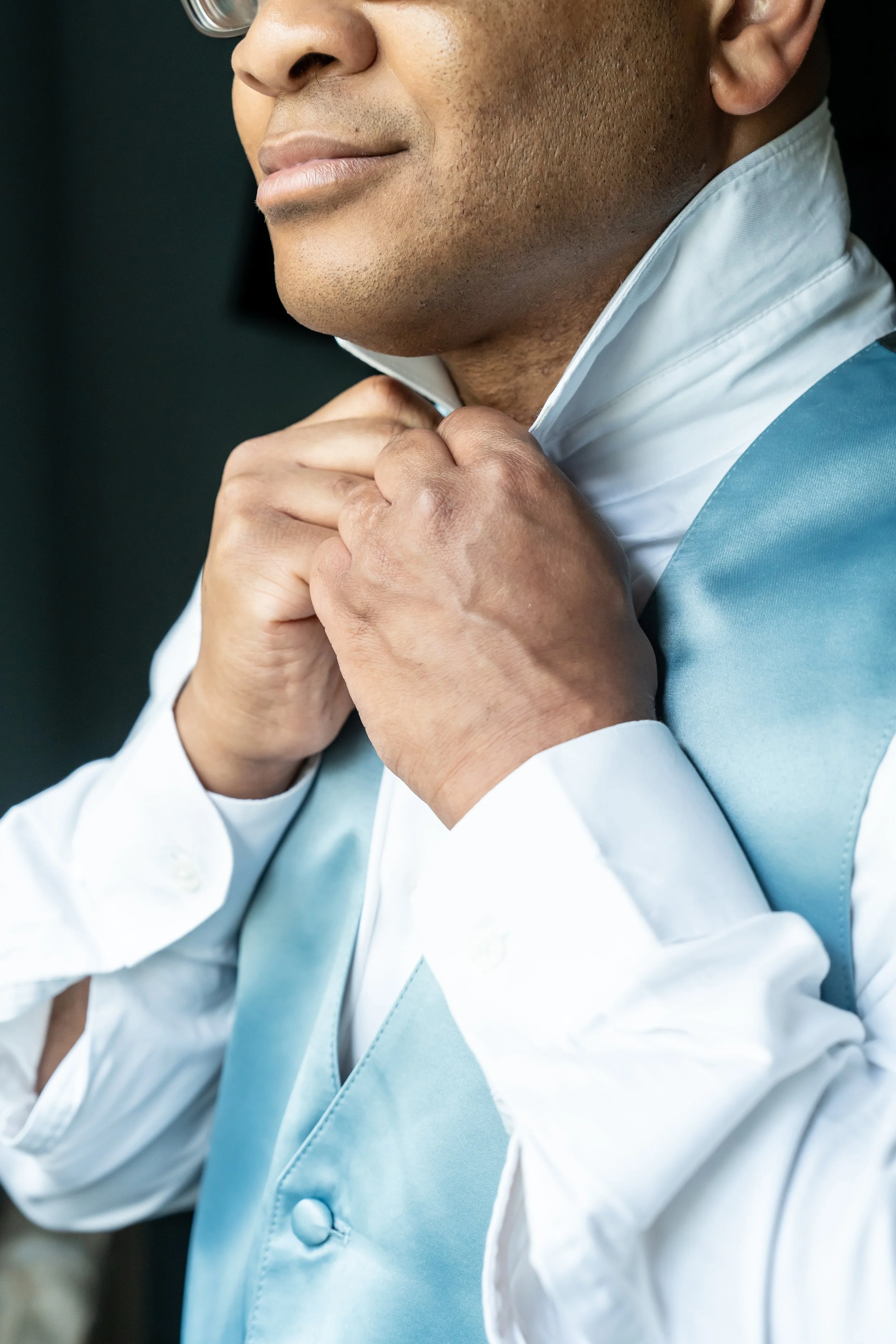 A man adjusting his light blue vest and white dress shirt collar.