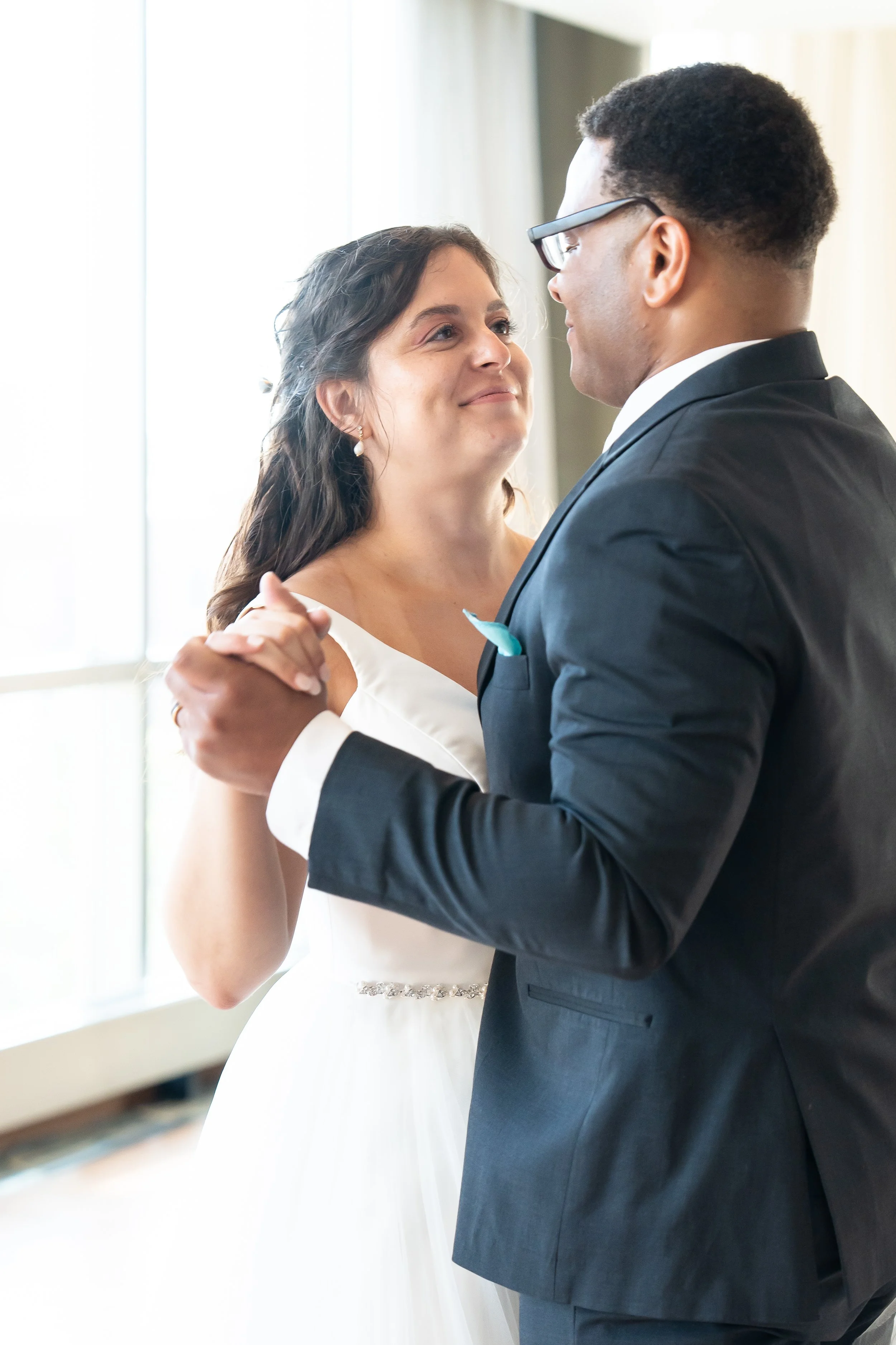 A couple dancing at a wedding reception, with the bride in a white dress and the groom in a dark suit, looking into each other's eyes.