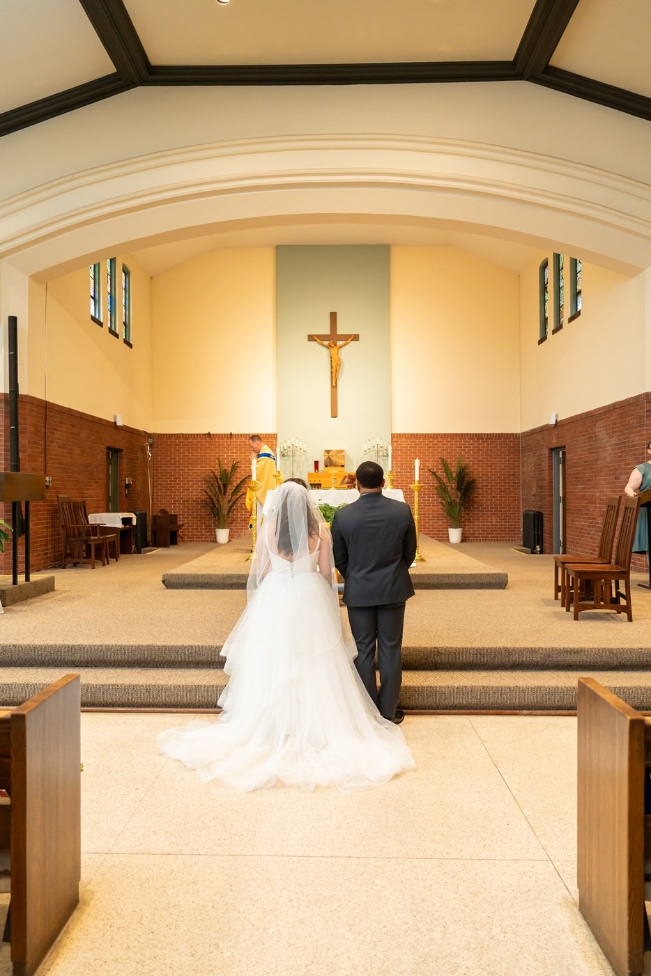 A bride and groom standing together at the altar in a church during their wedding ceremony, with a priest officiating.