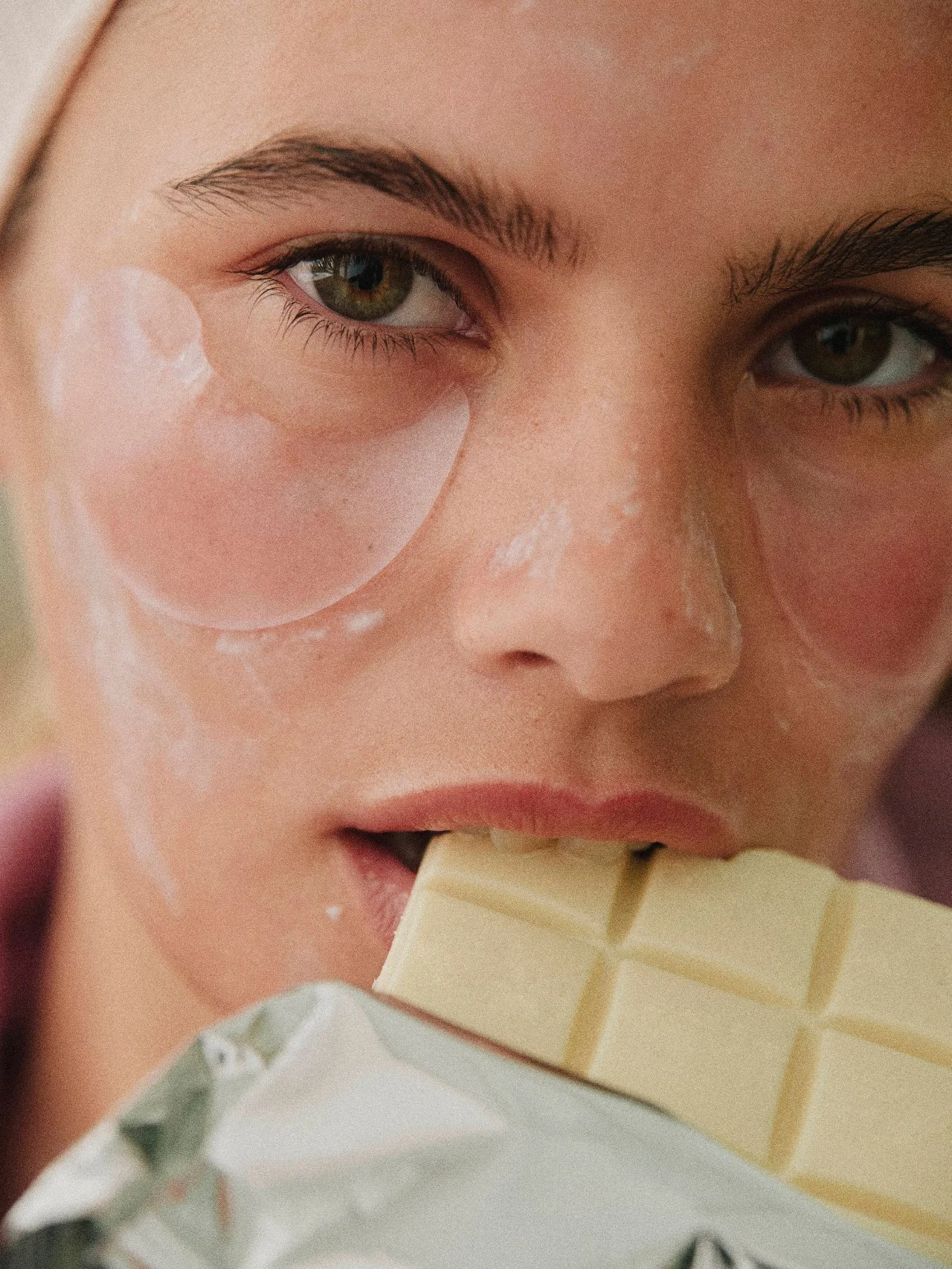 Close-up of a young woman's face with green eyes and freckles, licking a white chocolate bar.