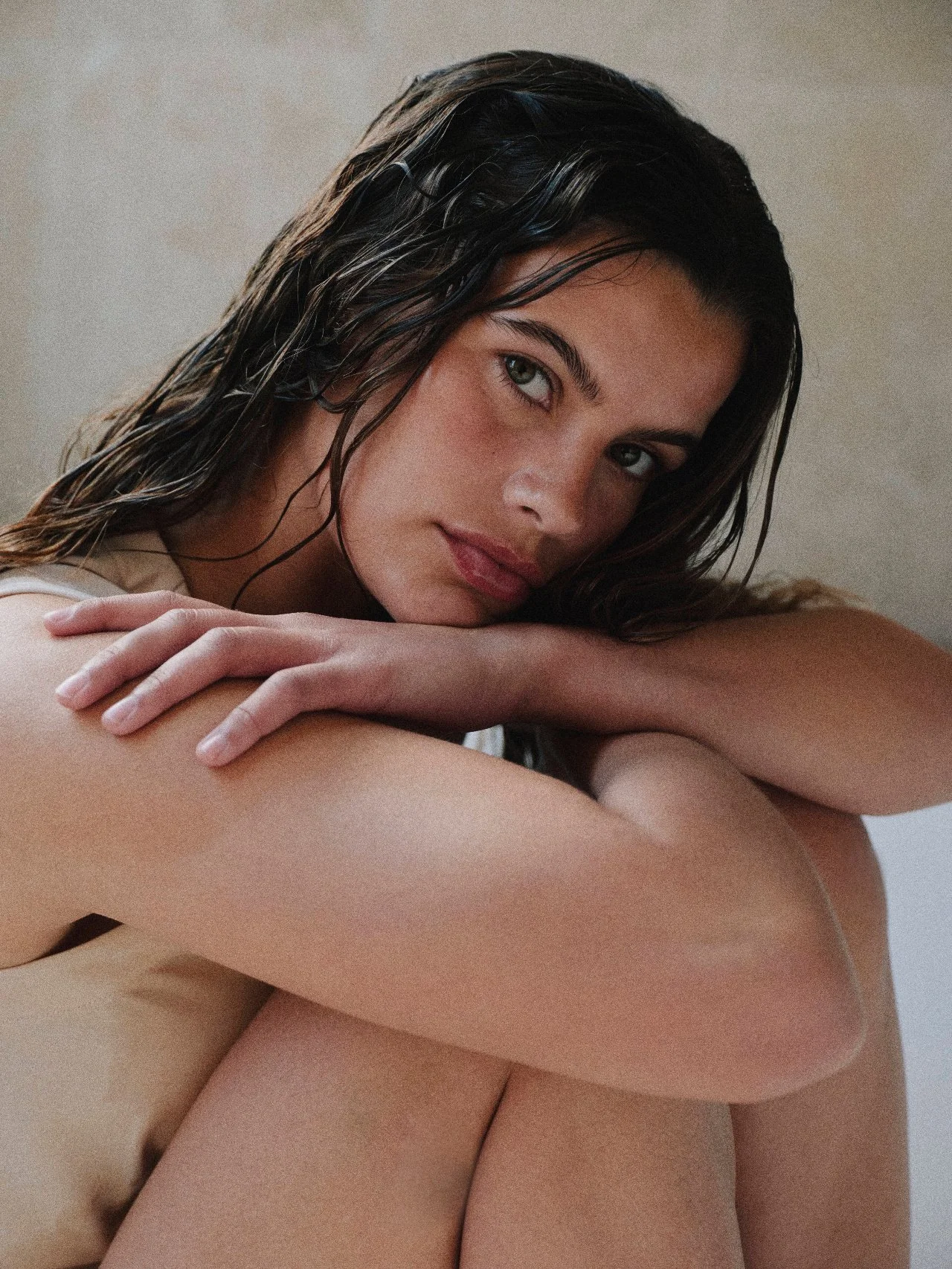 A woman with wet dark hair resting her head on her folded arms, looking directly at the camera.
