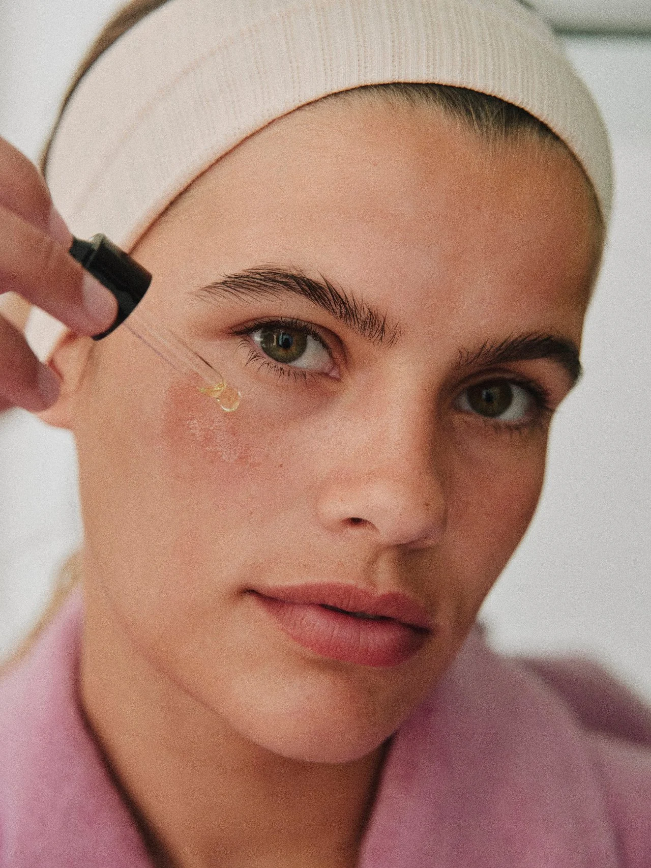 A person applying skincare serum to their face with a dropper.