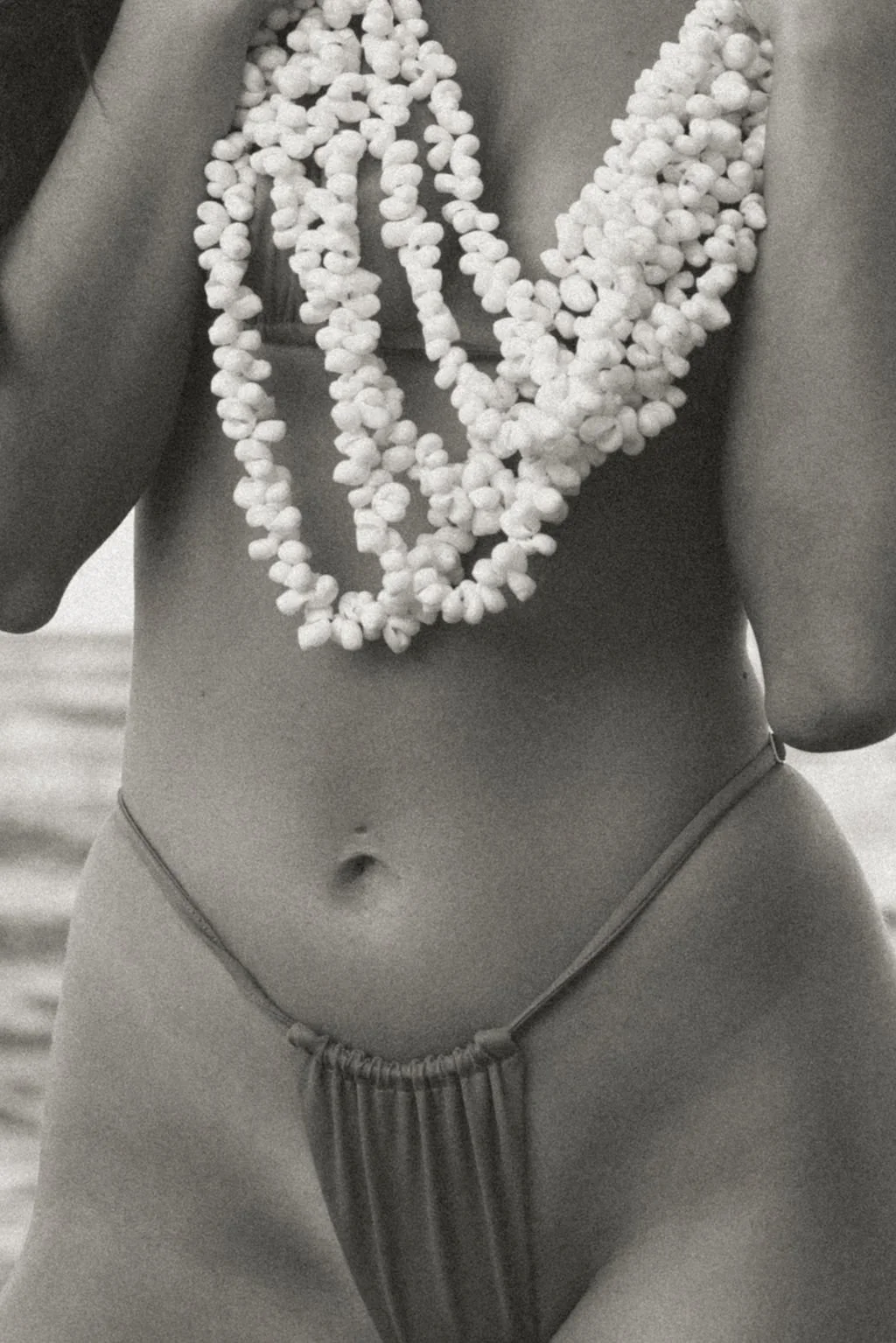 A person wearing a necklace made of small white objects and striped underwear, with their torso and lower body visible in black and white.
