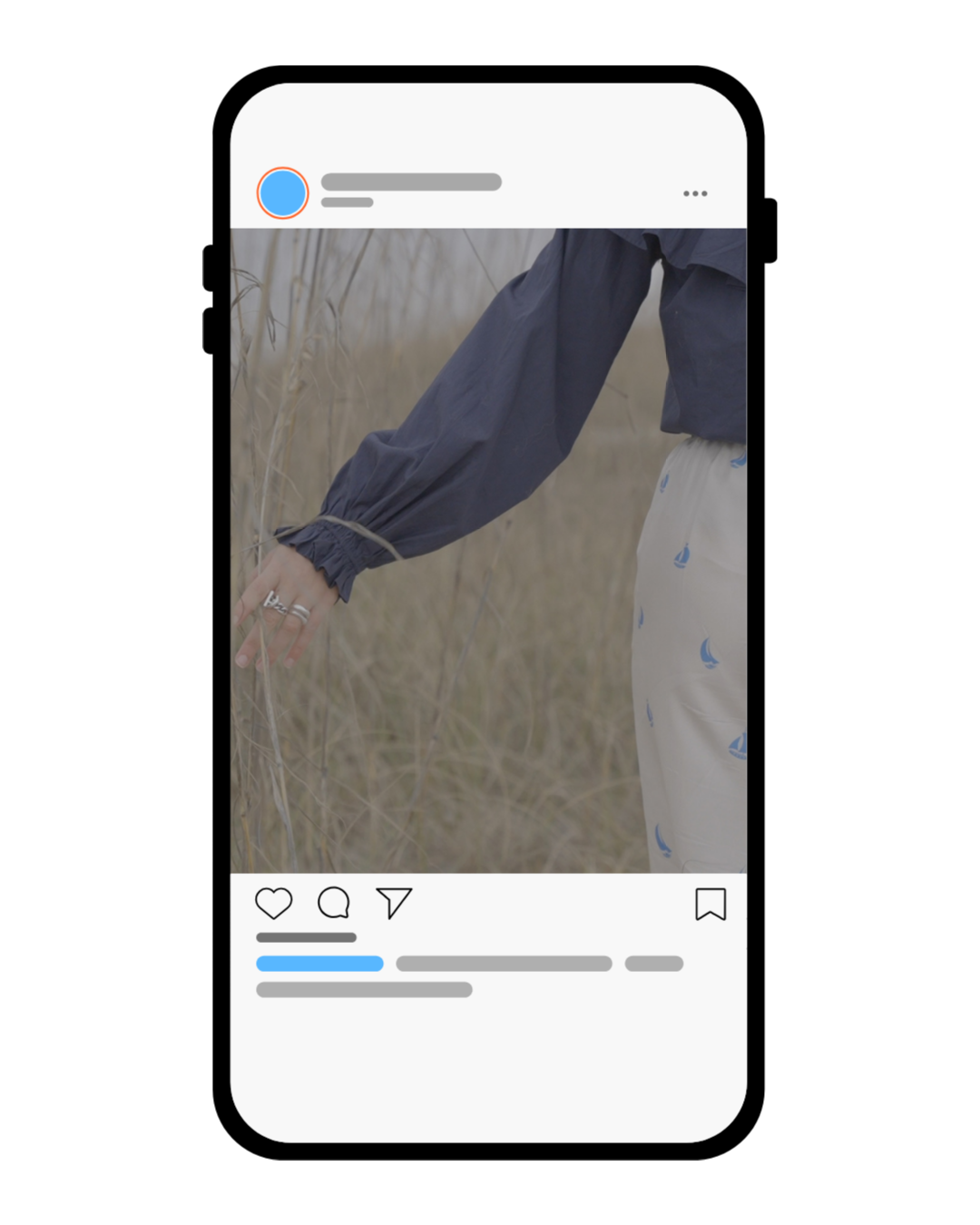 A person touching dry grass in a field, wearing a navy jacket and cream-colored pants with blue sailboat prints.