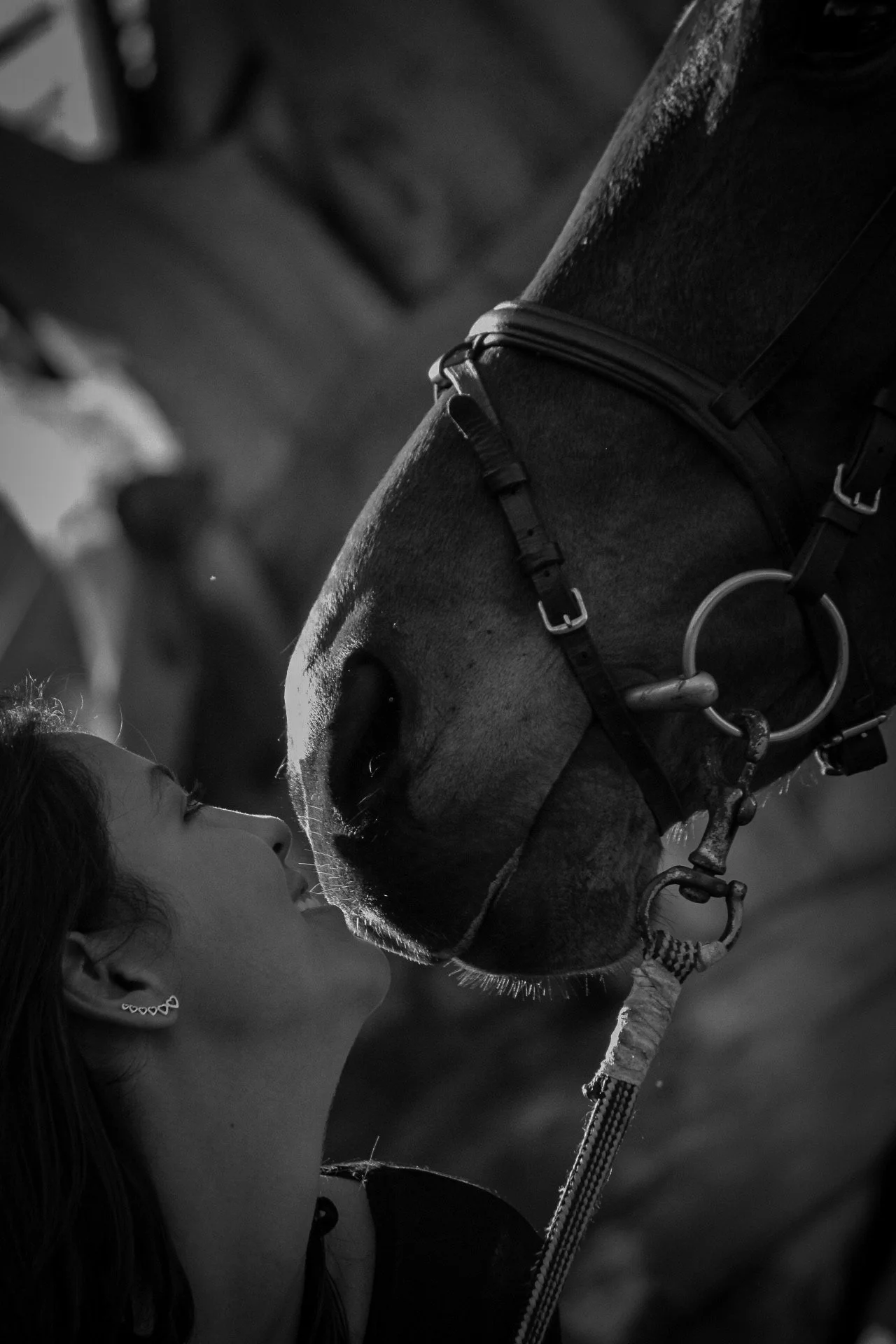 A woman with earrings is facing a horse, nose to nose, in a close and tender moment.