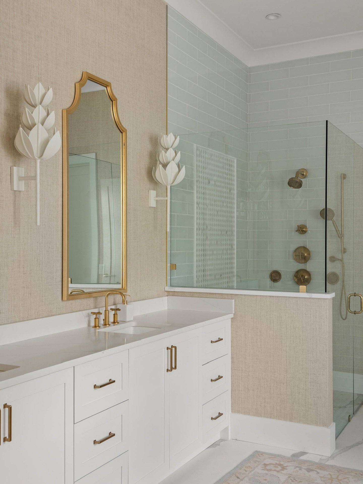 Primary bath of our dreams! There&rsquo;s nothing not to love about this mix of grasscloth wallpaper, warm gold accents, and delicate floral sconces.