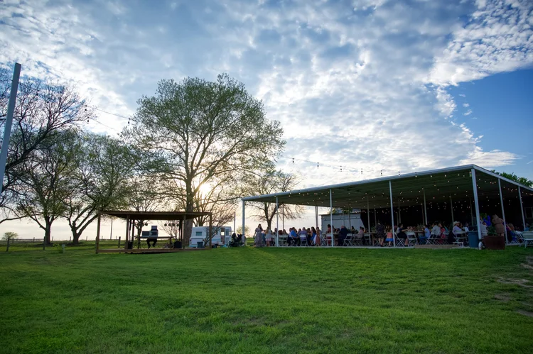Guests gathered under the reception pavilion beside a green lawn at sunset
