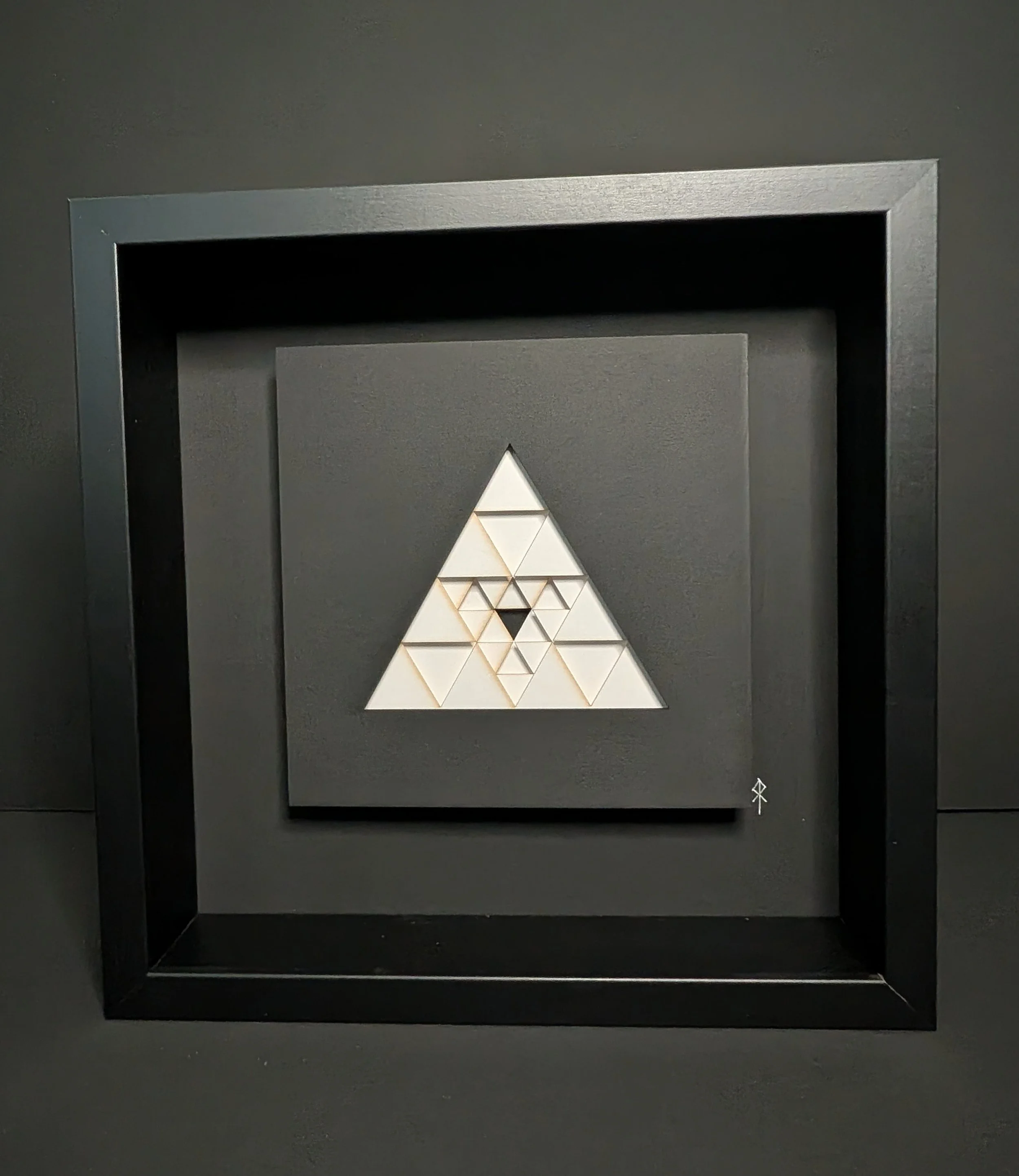 A framed geometric art piece featuring a large white triangle made of smaller triangles arranged inside a black frame.