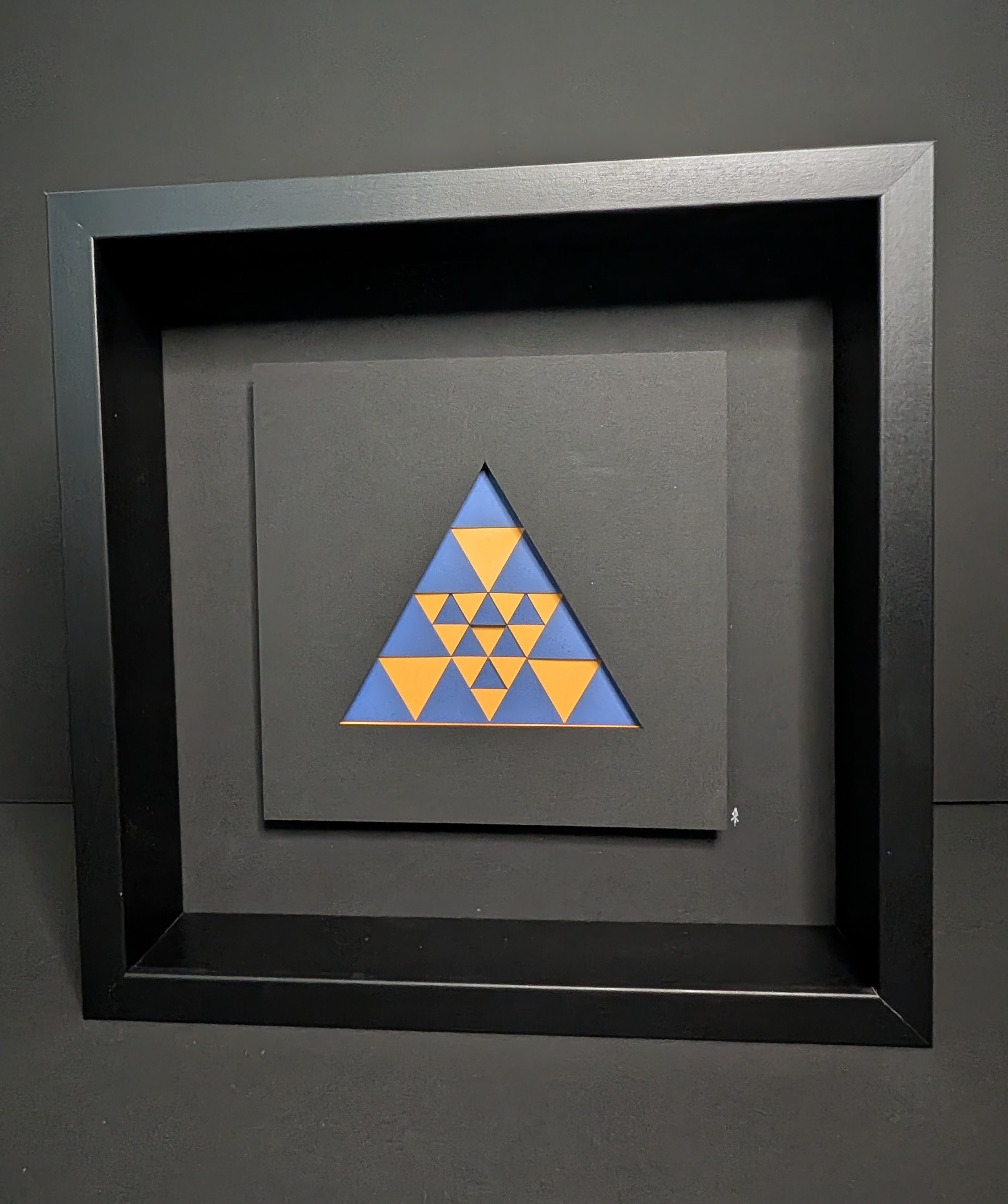 Framed triangular geometric art with yellow and blue triangular patterns on a black background.