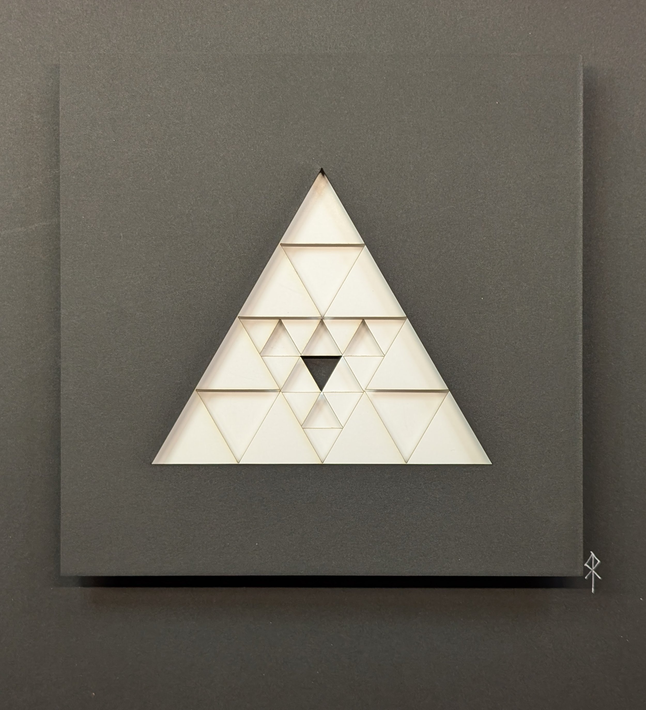 A wall art sculpture with white geometric triangle shapes within a large black square frame.