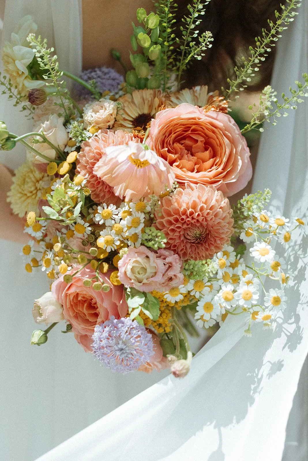 A close-up of a pastel-colored floral arrangement with pink roses, white daisies with yellow centers, and other seasonal flowers in soft shades of pink and orange.