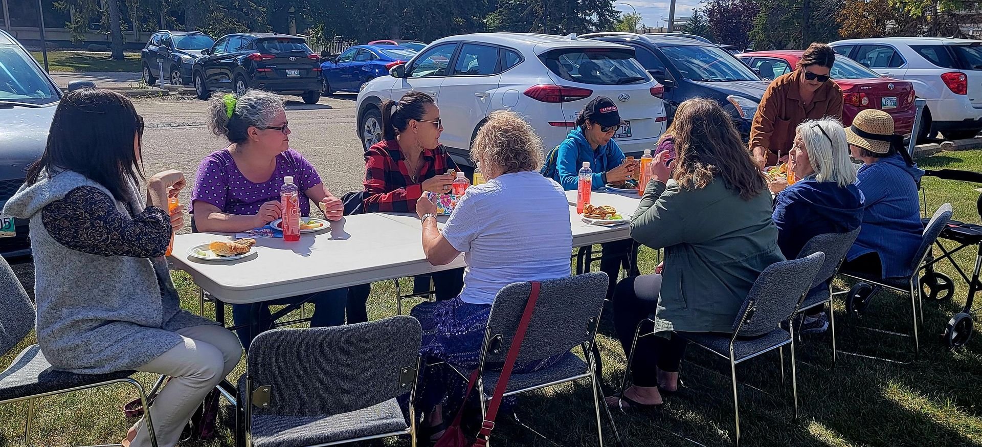 There are 9 women sitting at a table and one women standing at the end of the table. This OutReach team is celebrating with their 'end of summer' picnic.
