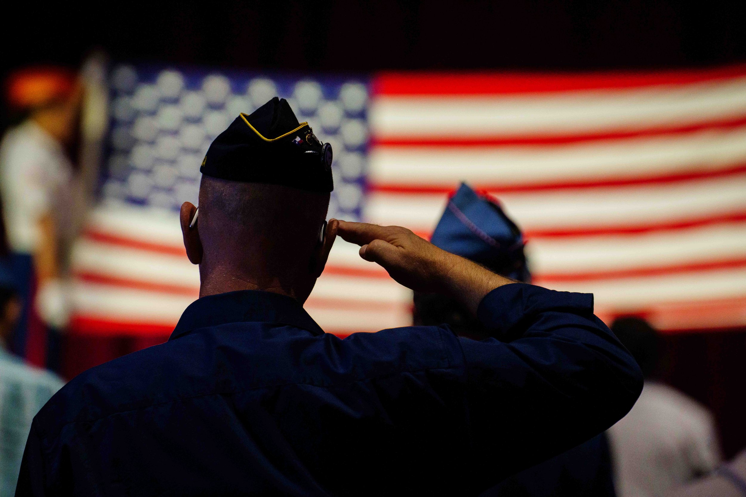  An American Legion member salutes the unfurled flag held by the Marine Corps Color Guard on the theater stage. The flag was refolded and presented to Jere Romano's wife, Martha Romano. 