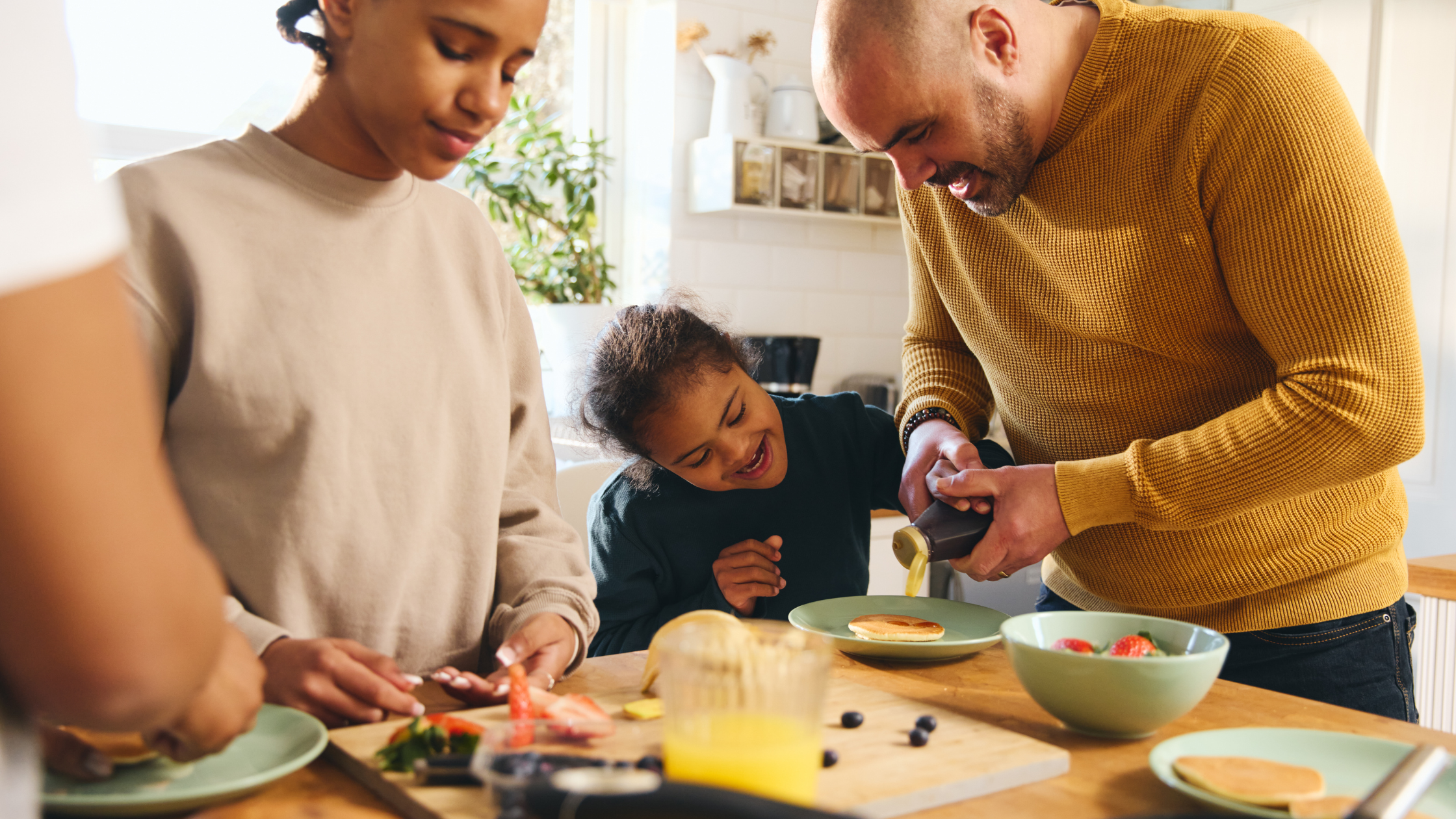 Three people at home in the kitchen preparing pancakes.