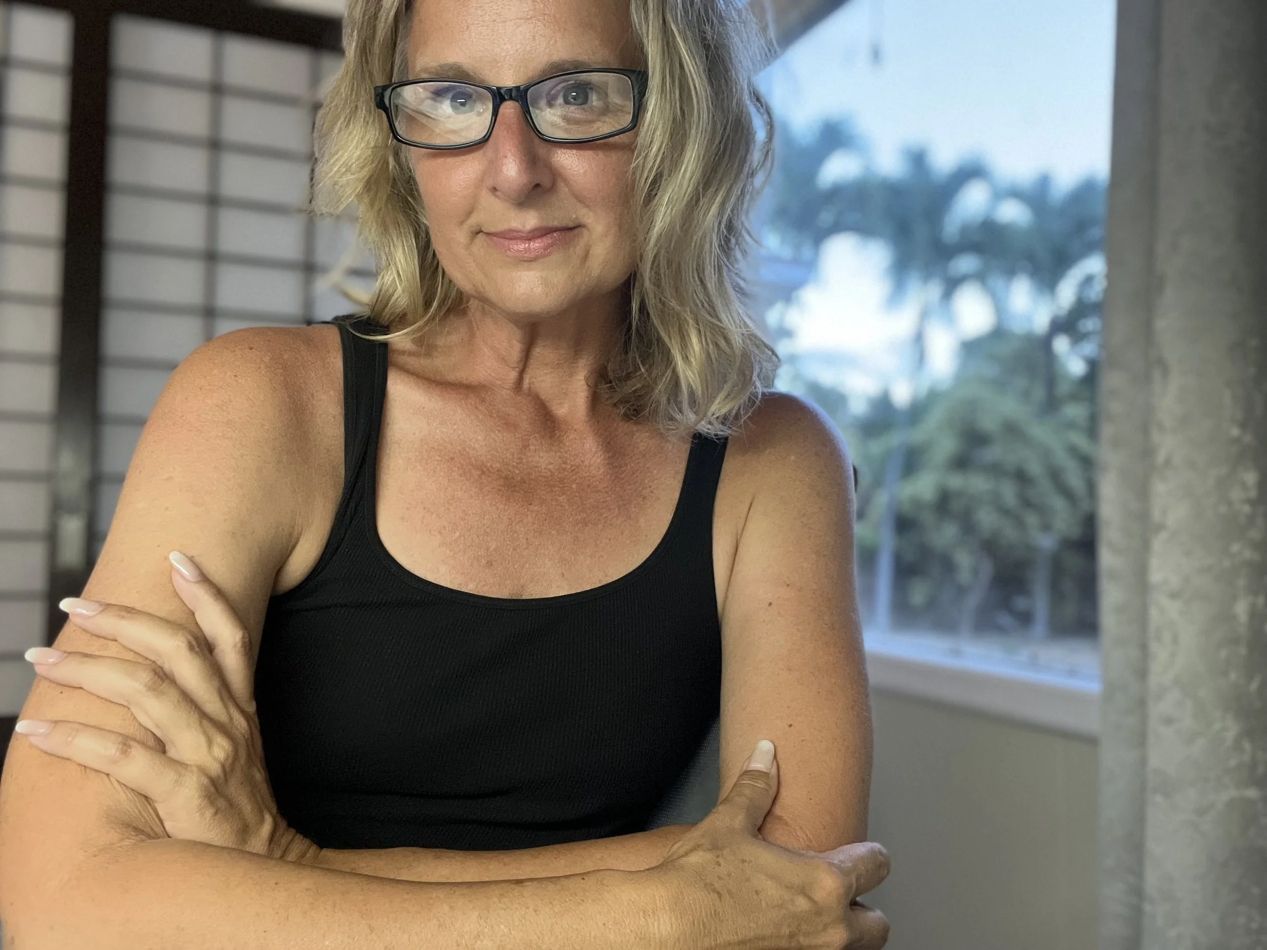 Author SJ Hodges Sitting in front of a window in reading glasses