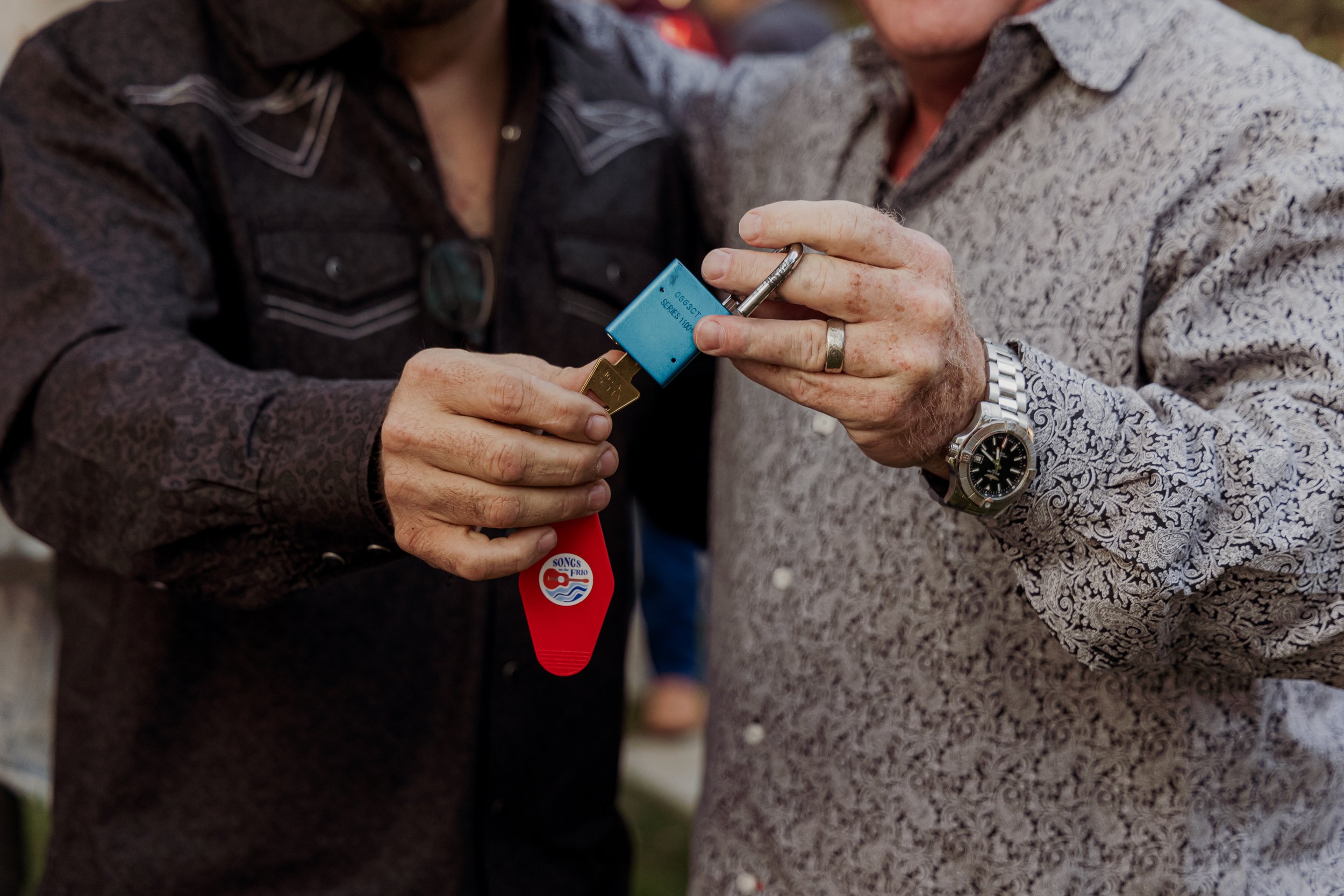 Two people exchanging a set of keys with a blue lock at an outdoor event.
