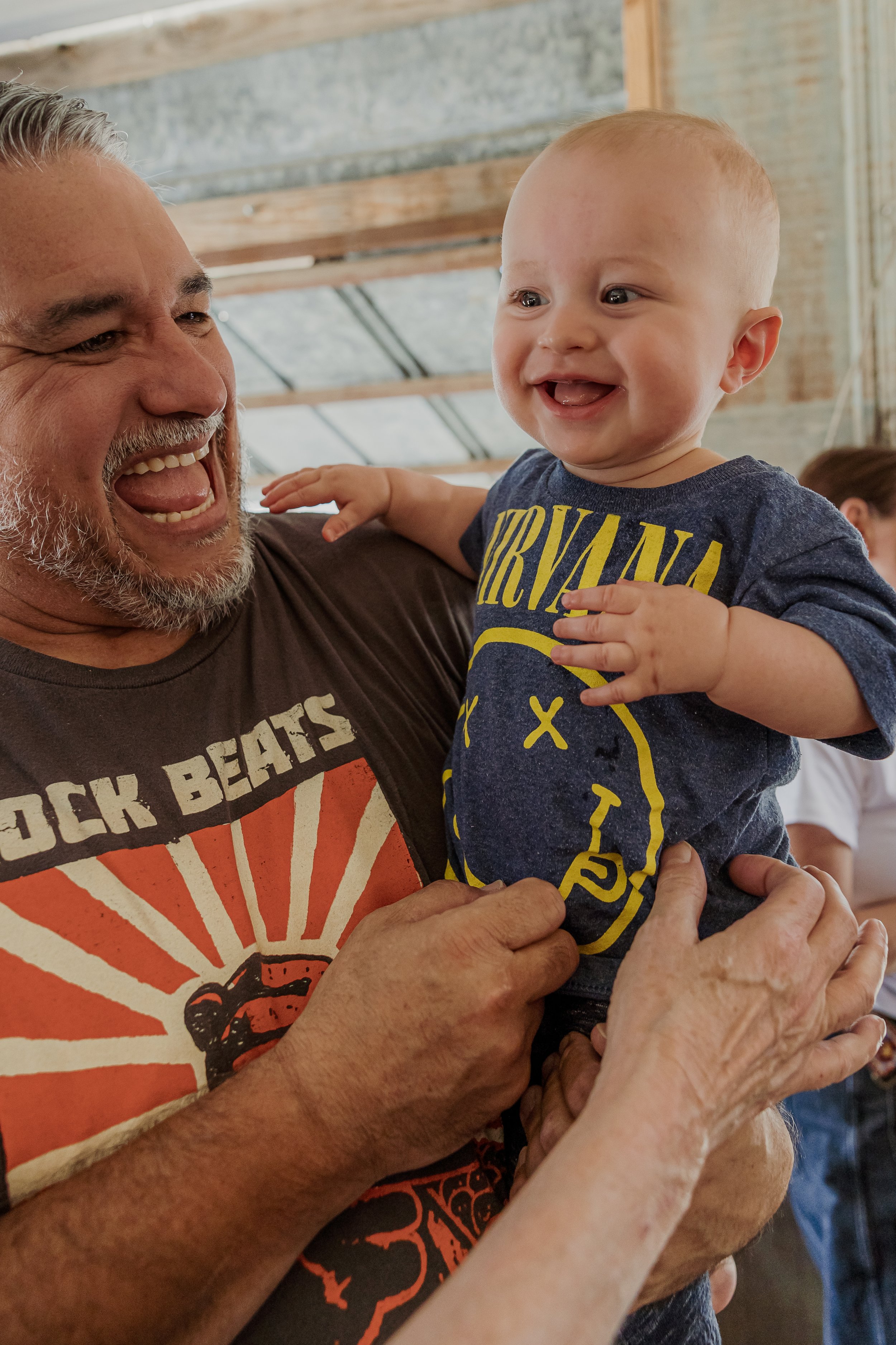 A smiling older man holding a happy baby boy dressed in a Nirvana t-shirt