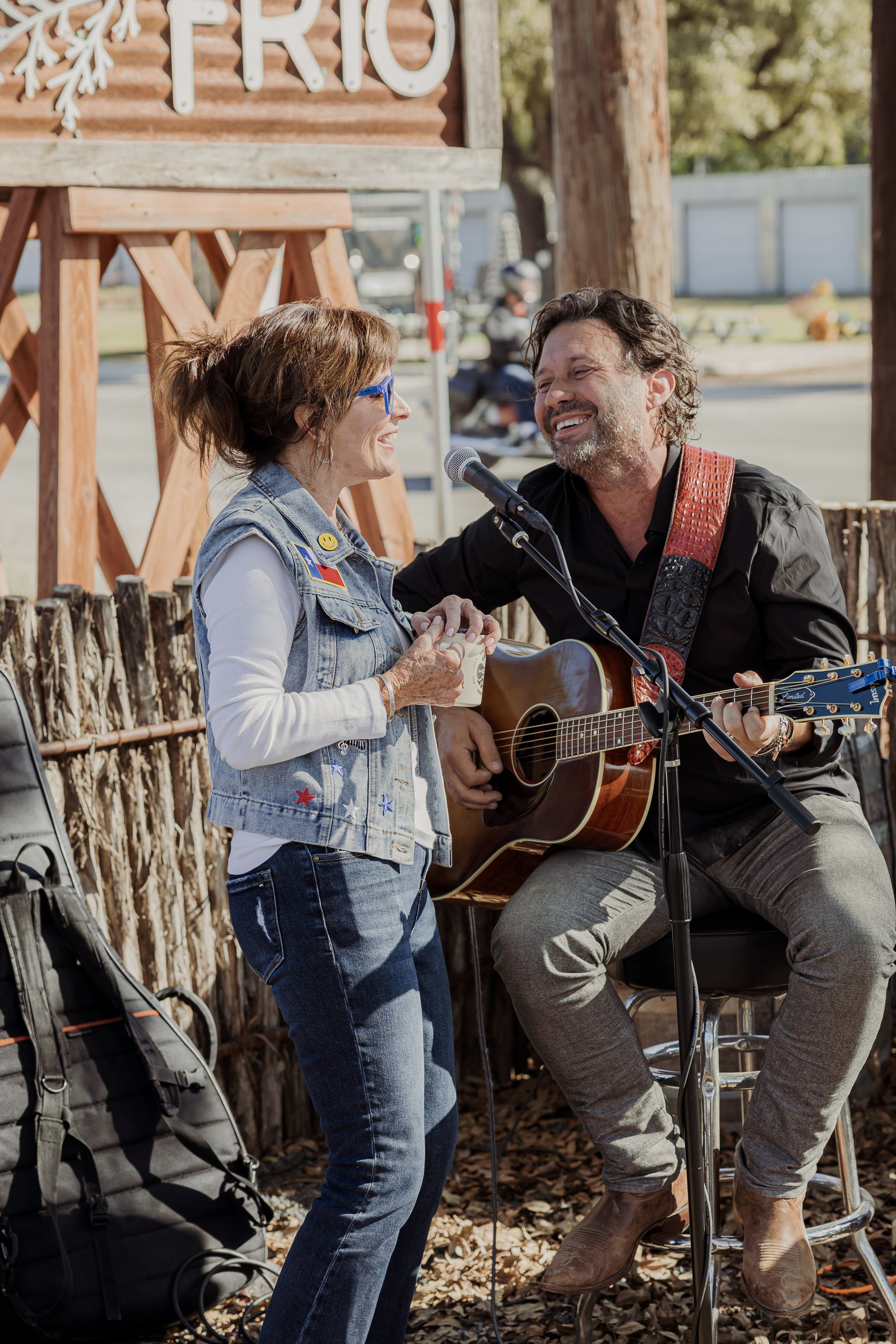 A woman singing with a man playing a guitar outdoors, both smiling and enjoying music.