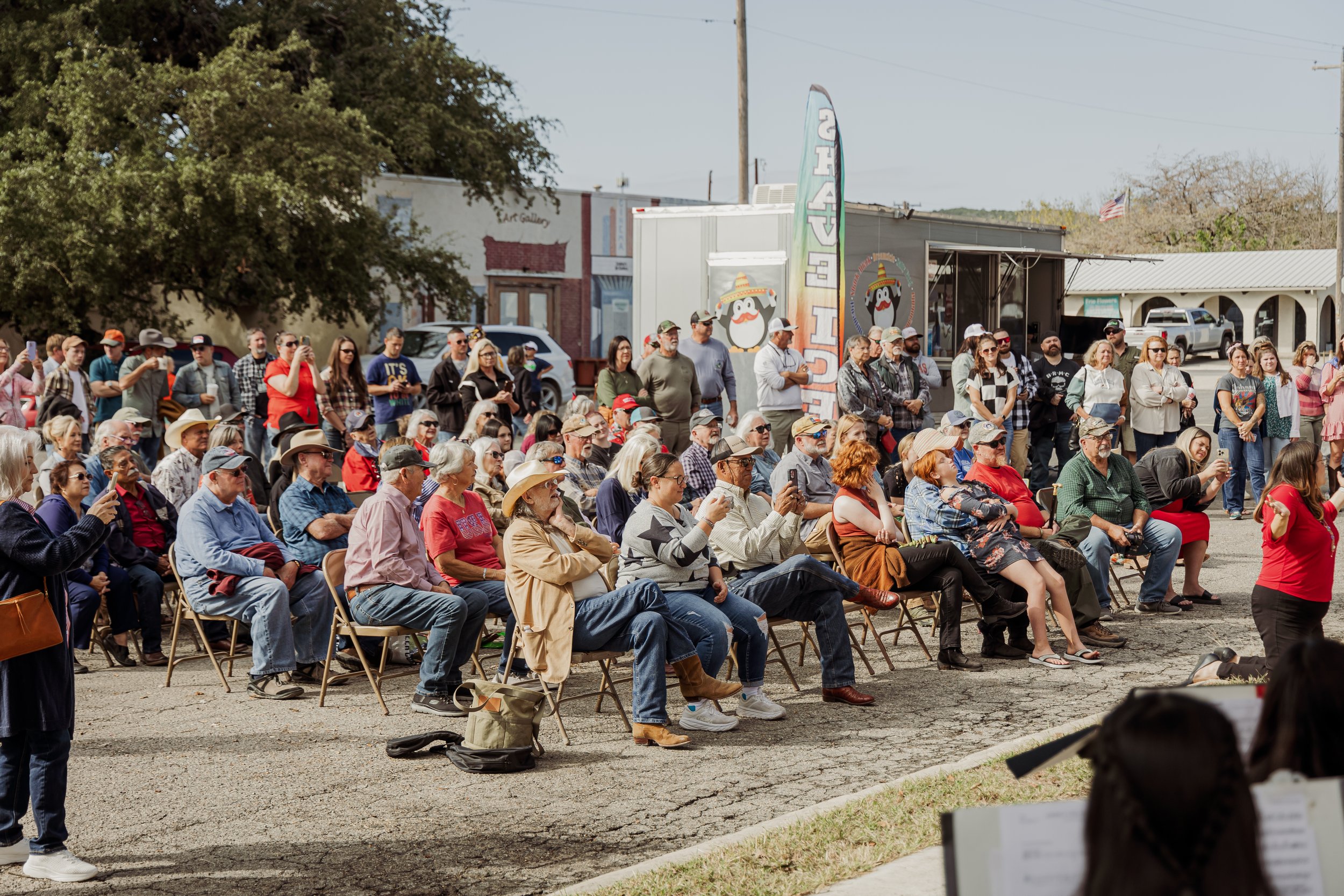 An outdoor event with rows of seated and standing spectators watching a performance or presentation.