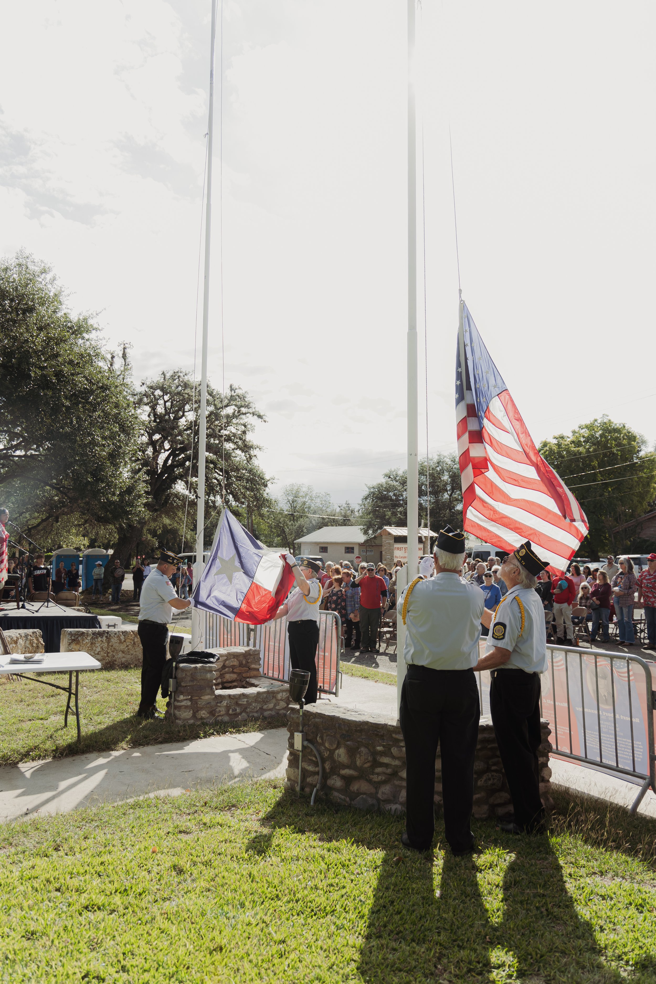 Veterans are raising the American flag during a patriotic ceremony, with a crowd of onlookers gathered nearby.