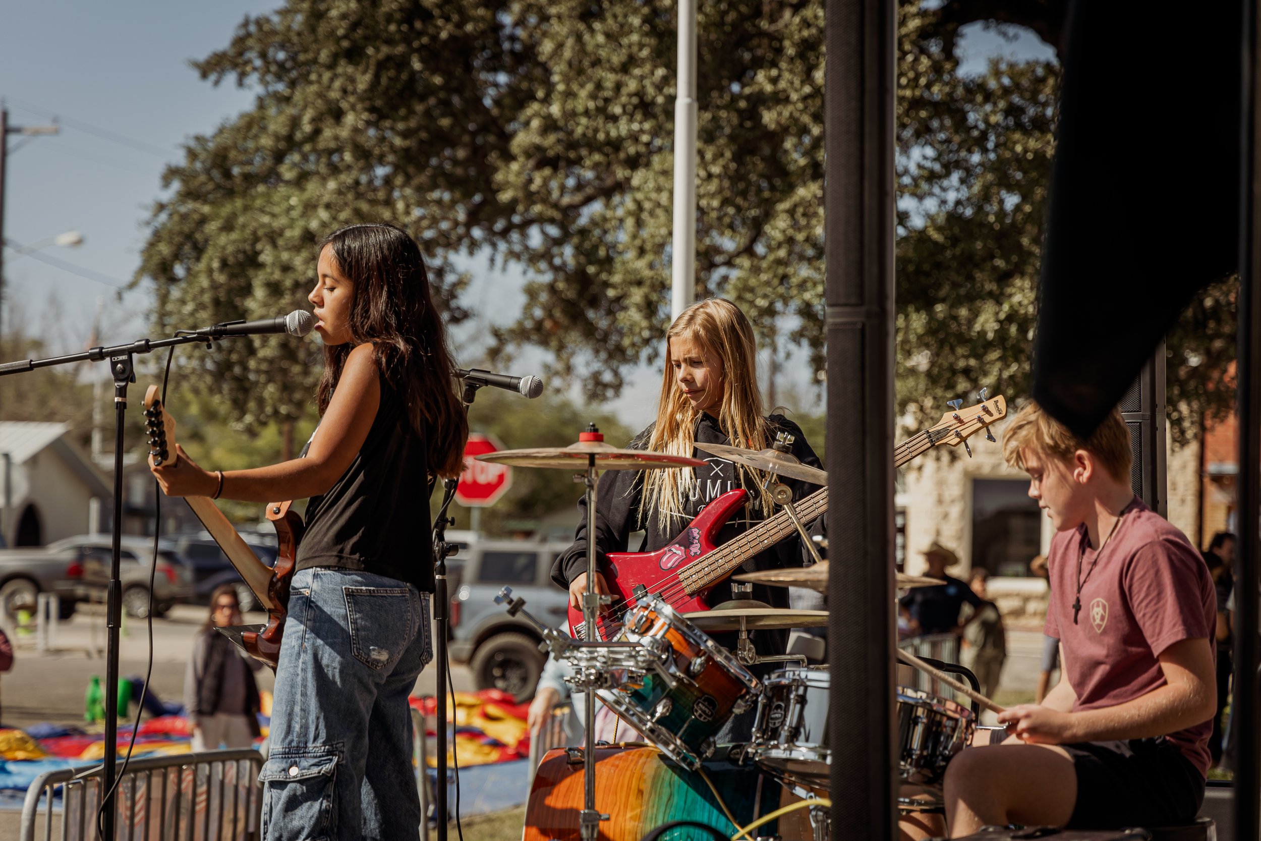 Three young female musicians playing instruments outdoors during a performance on a sunny day.