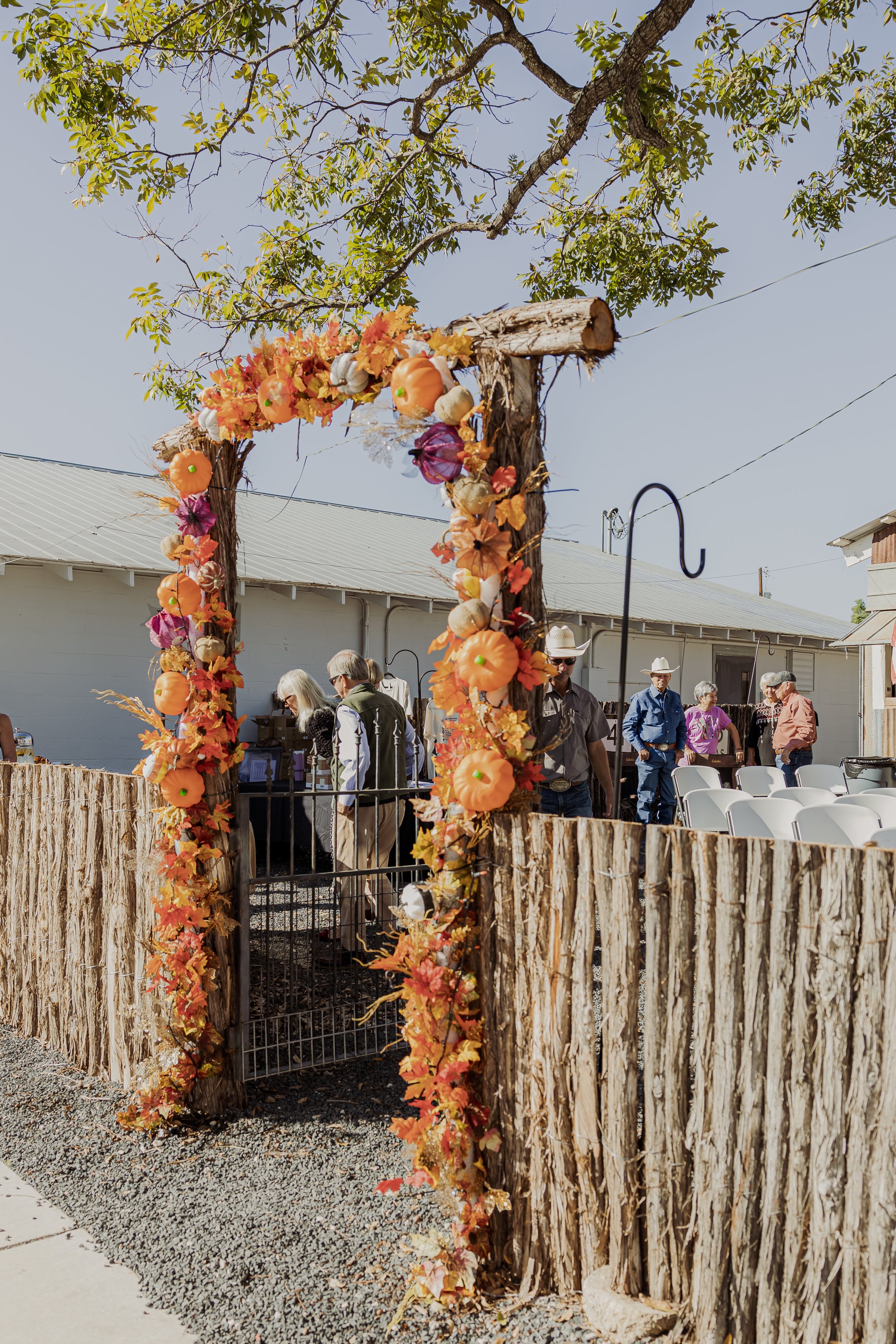 Decorated wooden arch with autumn-themed pumpkins and leaves, set up outdoors with a group of people in the background