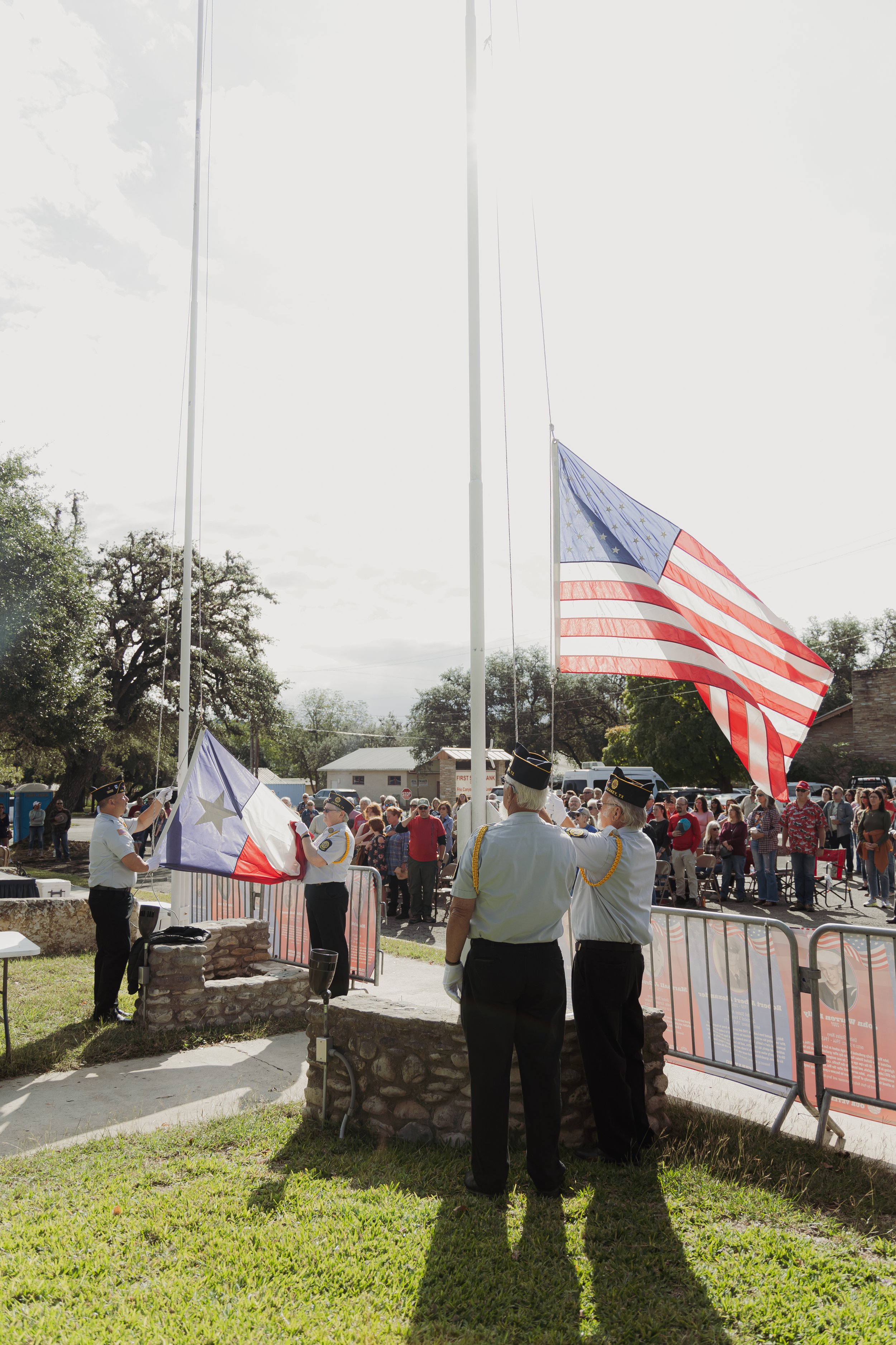 Flag ceremony with four uniformed individuals raising flags, surrounded by a crowd in an outdoor setting during daytime.