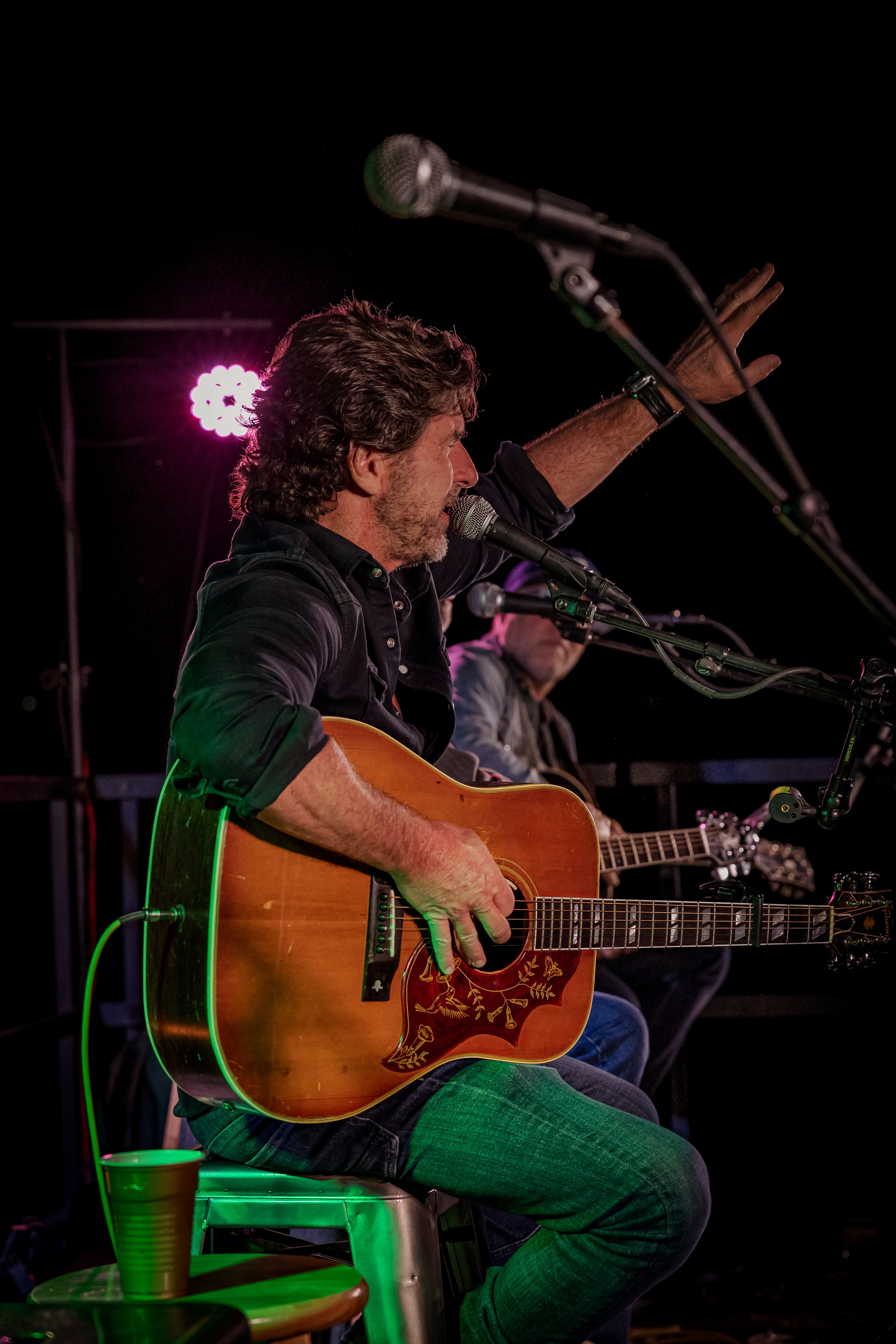 Man playing acoustic guitar, singing into microphone during live performance at night.