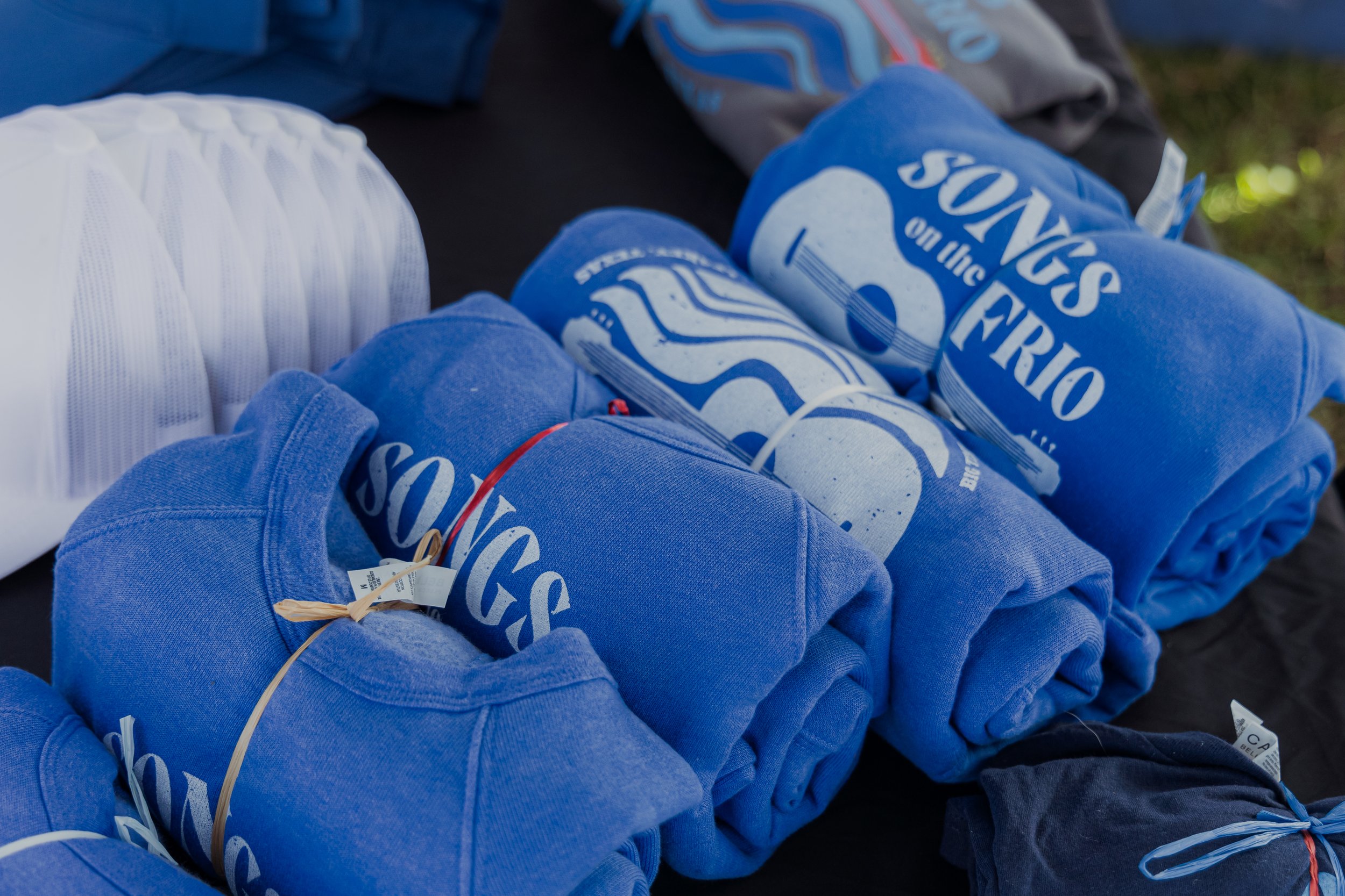 Rolled and folded blue t-shirts with white text, and a white circular object on black fabric surface.