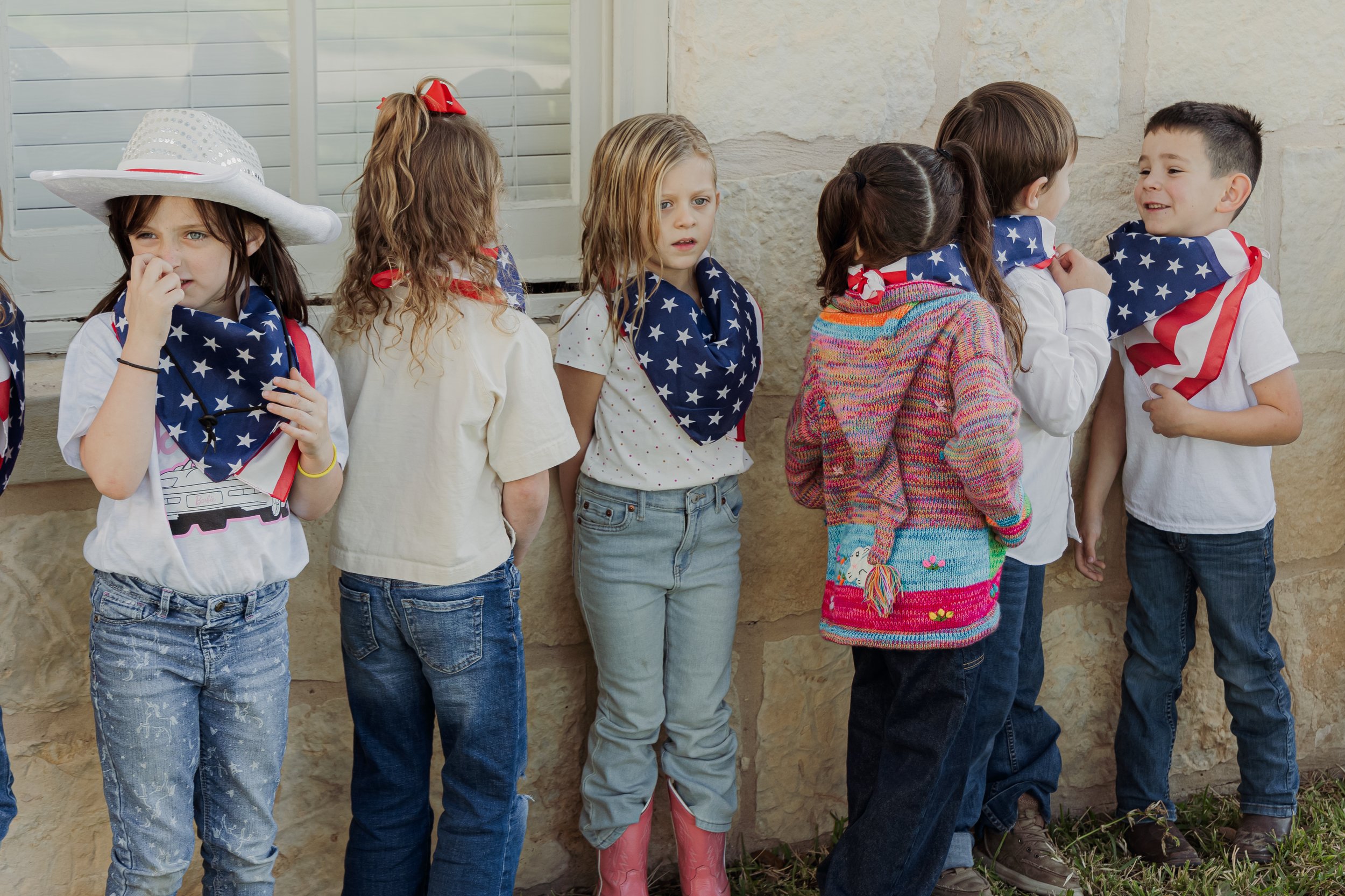Children standing in line outside, wearing patriotic bandanas and casual clothing.