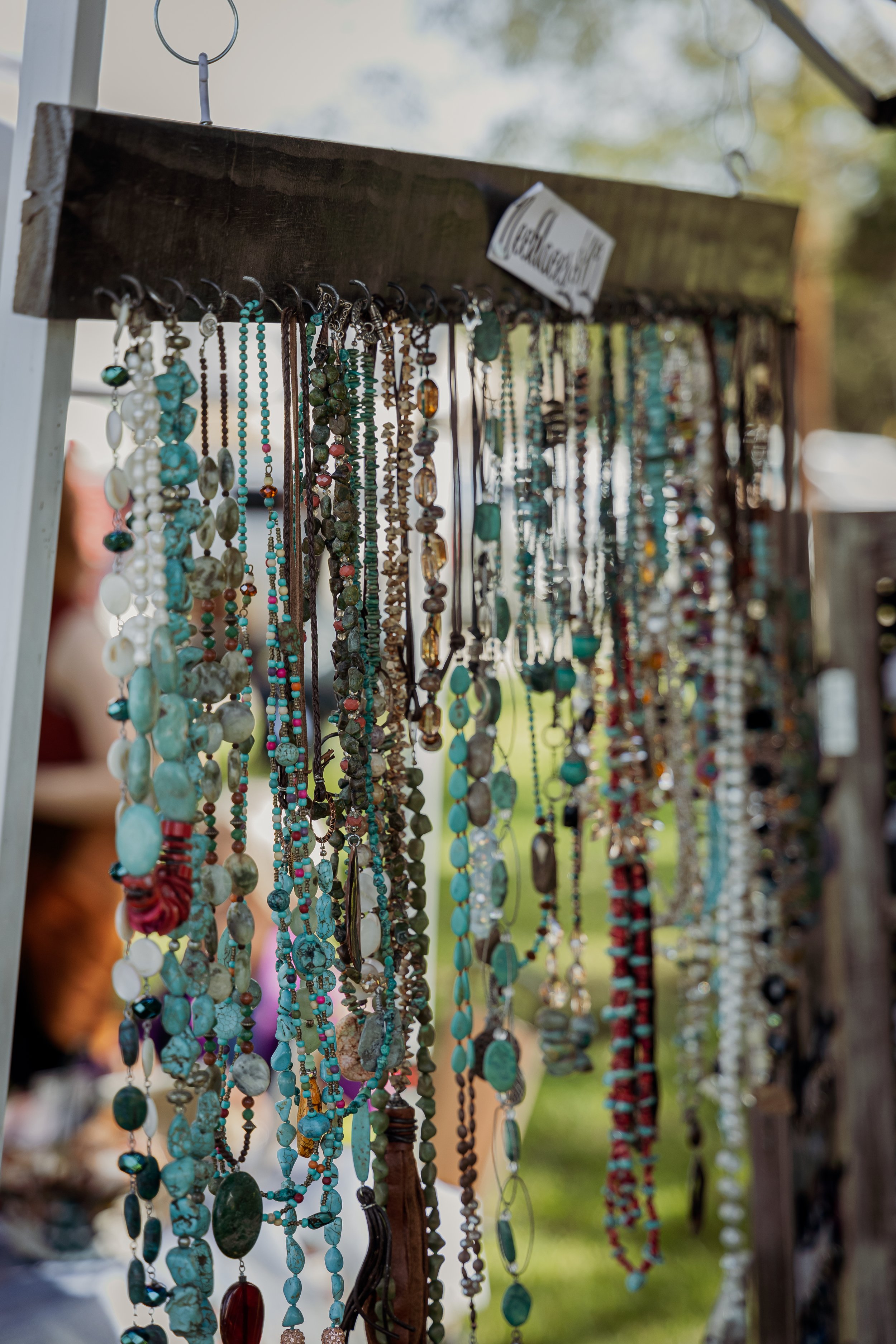 Collection of various necklaces hanging on a wooden display at an outdoor market.