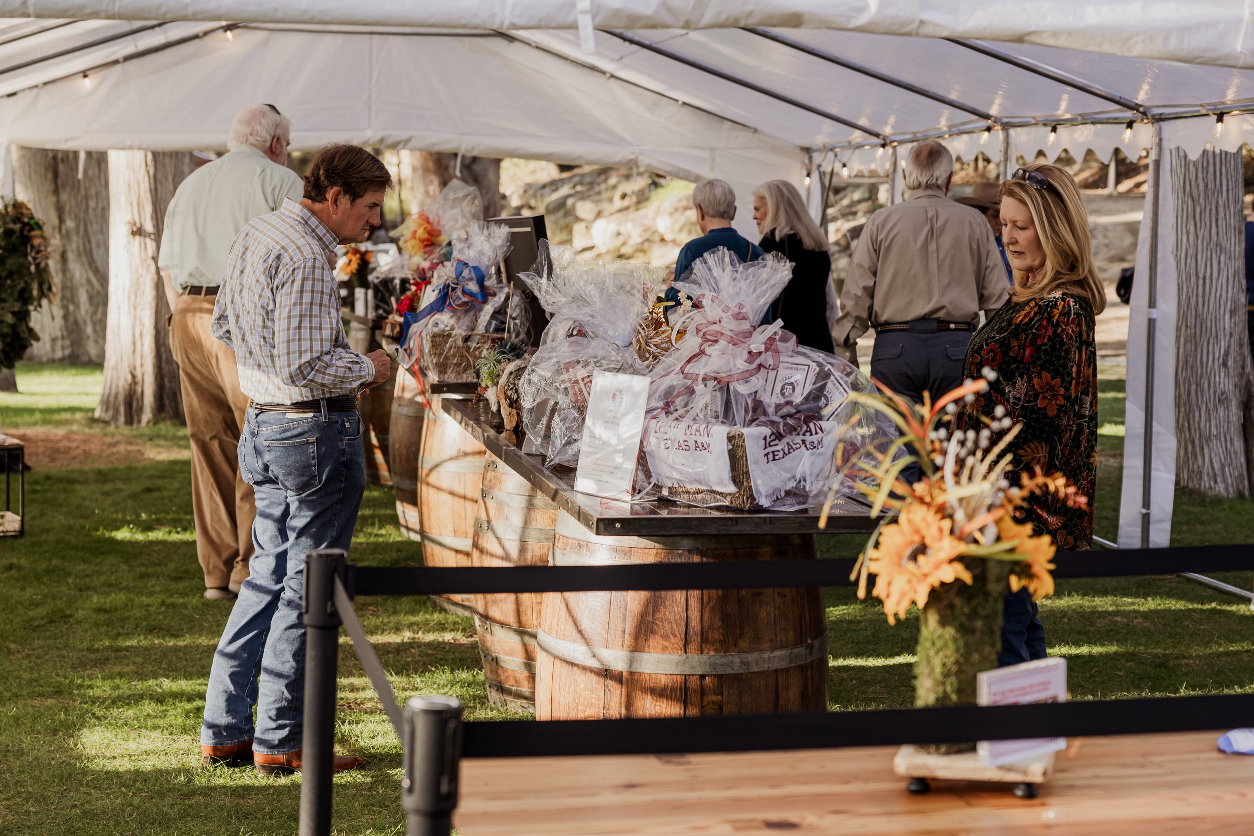 People browsing a gift basket display under a white tent at an outdoor event or market.