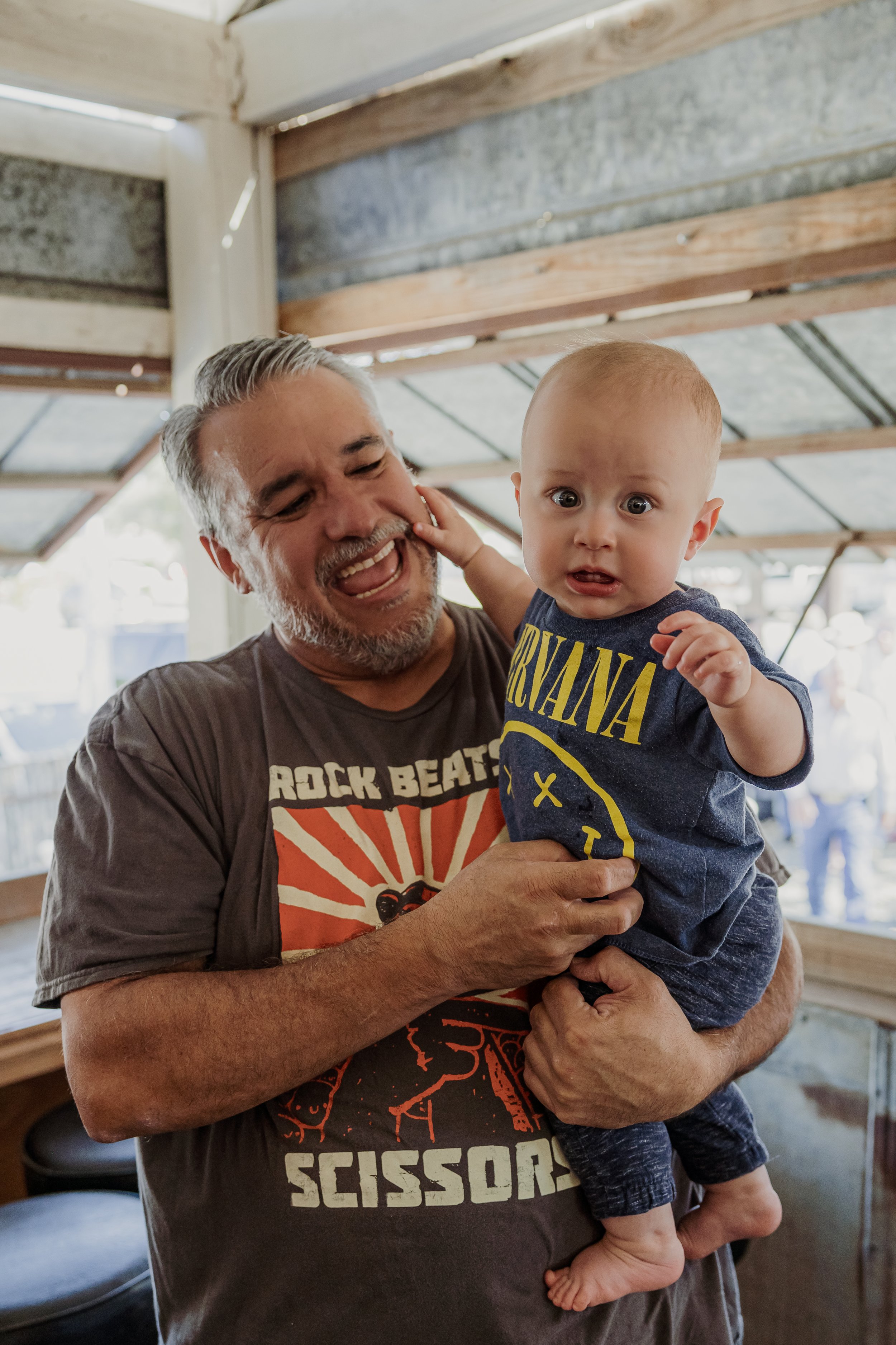 A man holding a surprised baby inside a rustic wooden structure.