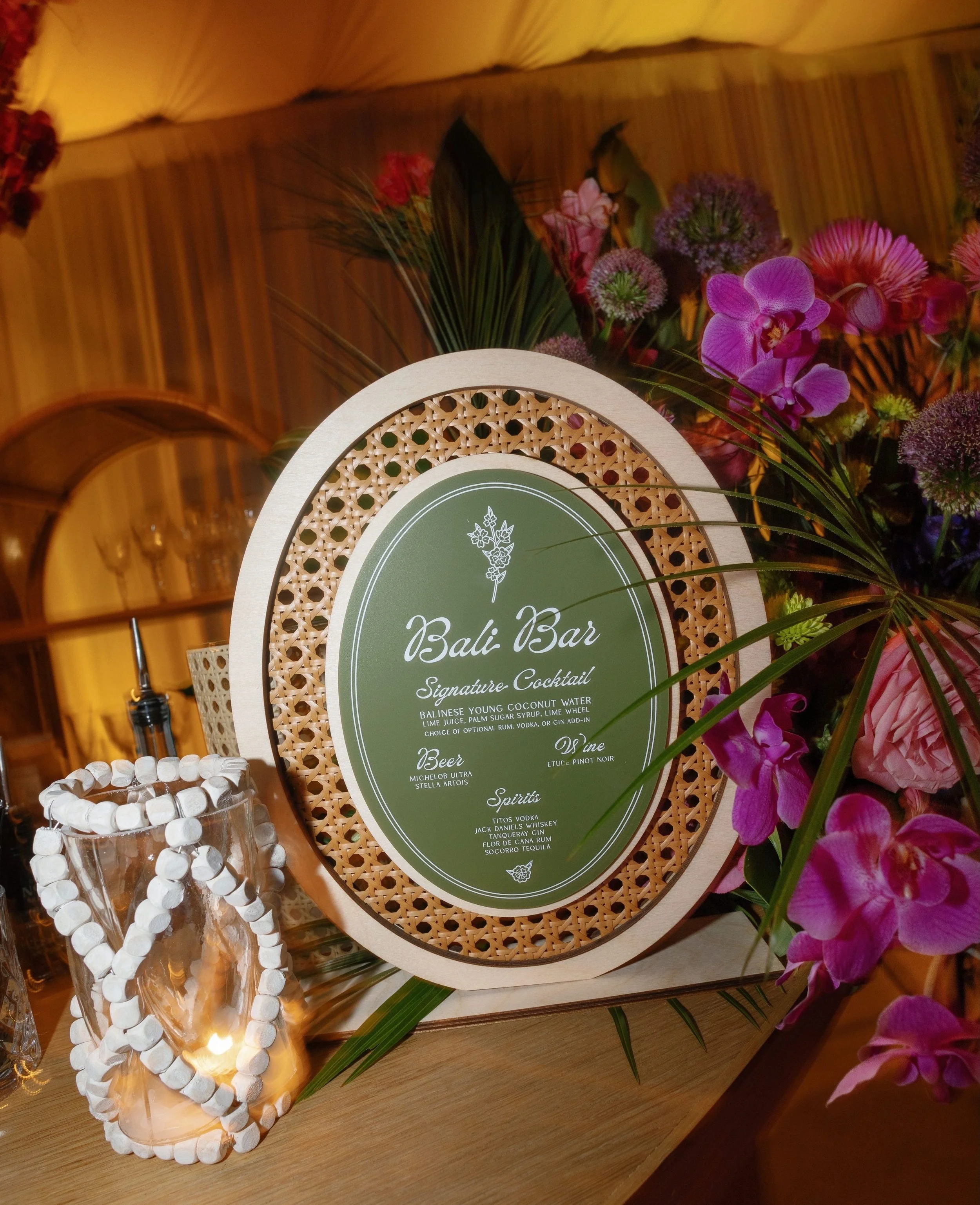 A Bali inspired celebration for Megan and Joshua, grounded in natural texture and warm, organic materials. An oval acrylic bar sign took center stage, layered with rattan and wood elements that brought an easy, coastal feel to the space. A relaxed ye