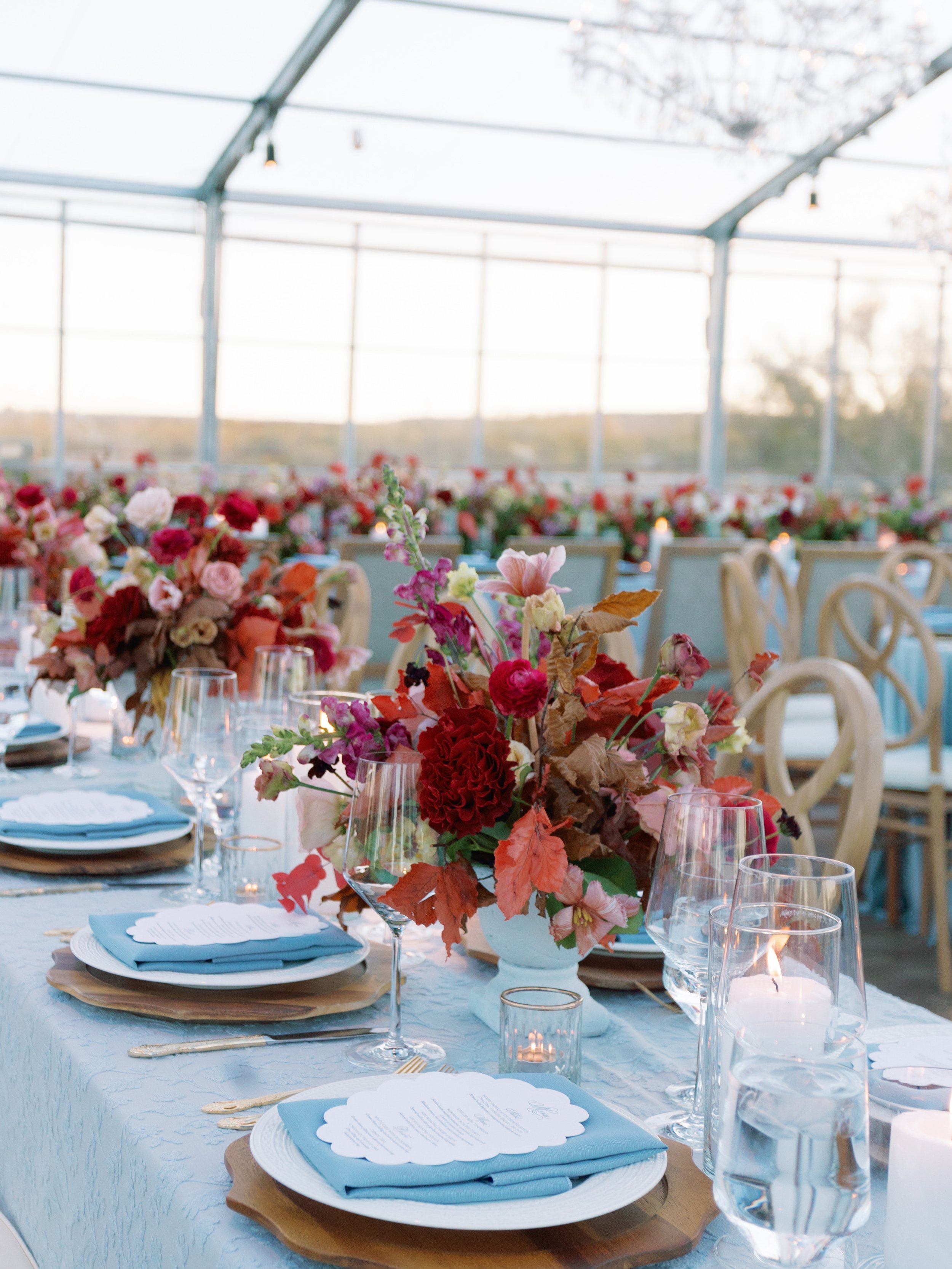 Clear Top Tent Private Estate Ranch Wedding Reception Entrance with Red and Burgundy Florals, Blue Linens and Chandeliers and Custom Blind Embossed and Blue Letterpress Scalloped Menus