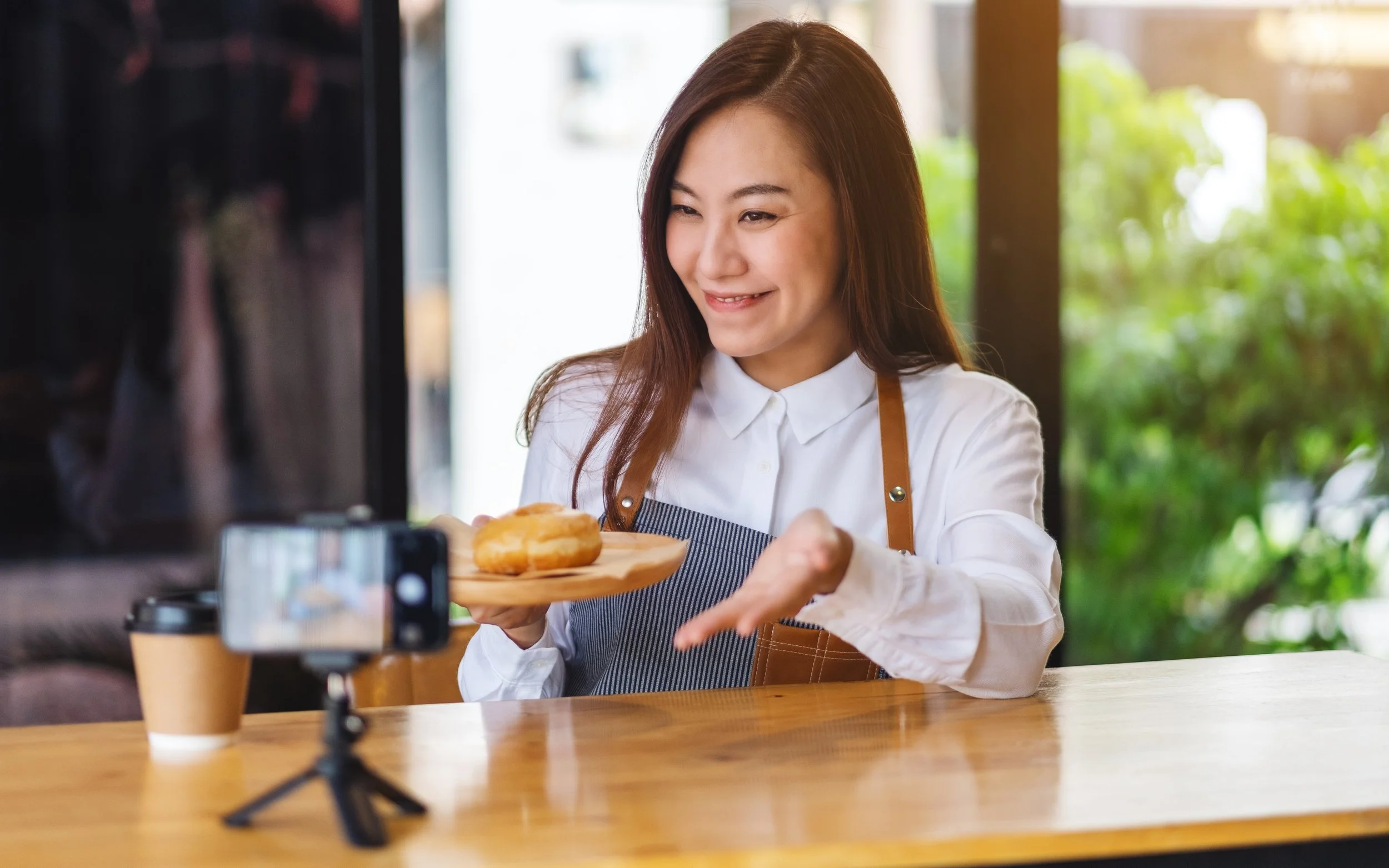 A women holding a plate of food at a phone filming on a tripod