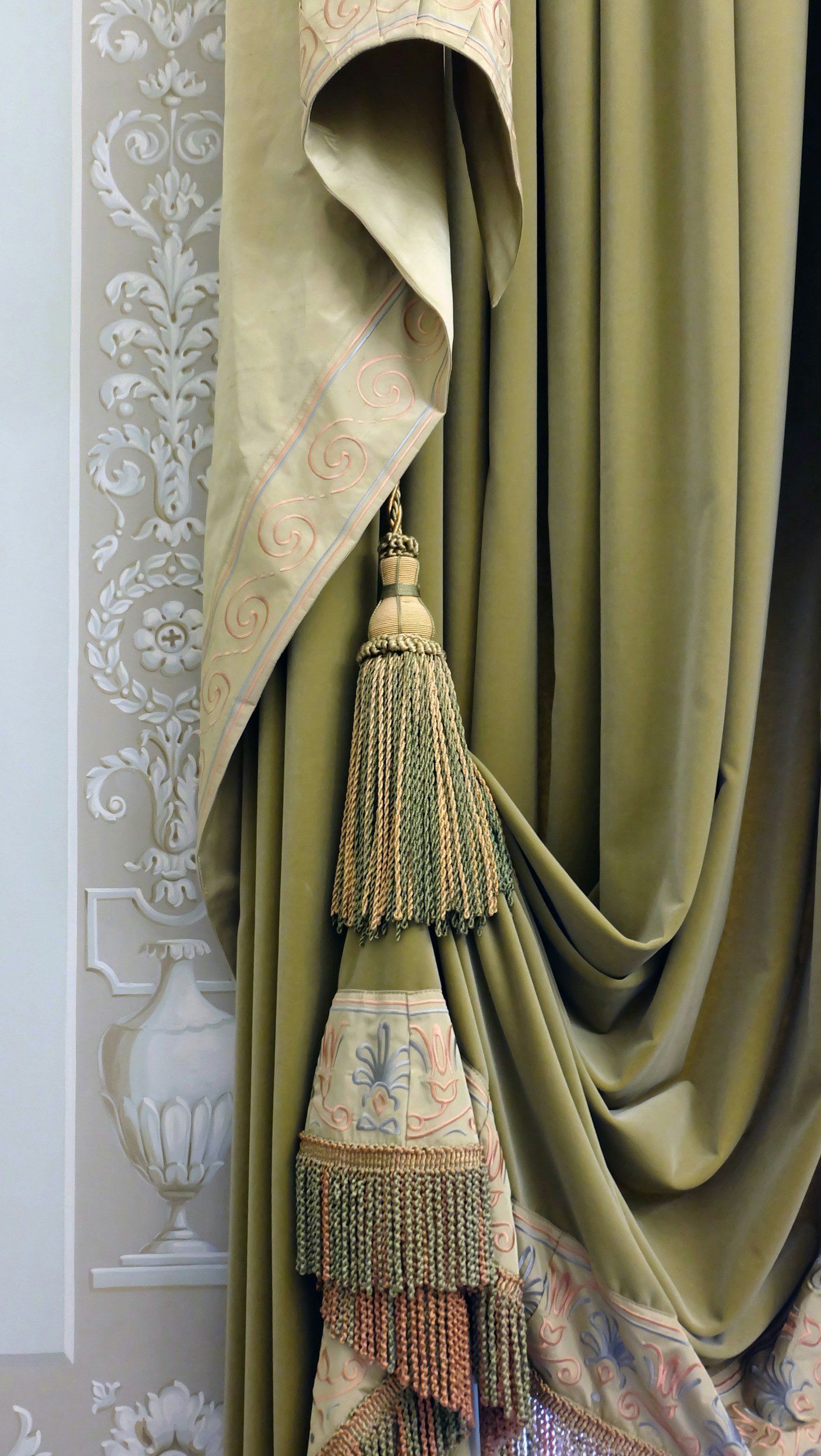 Decorative curtains with intricate embroidery and tassels, alongside a wall with ornate floral and scrollwork design.