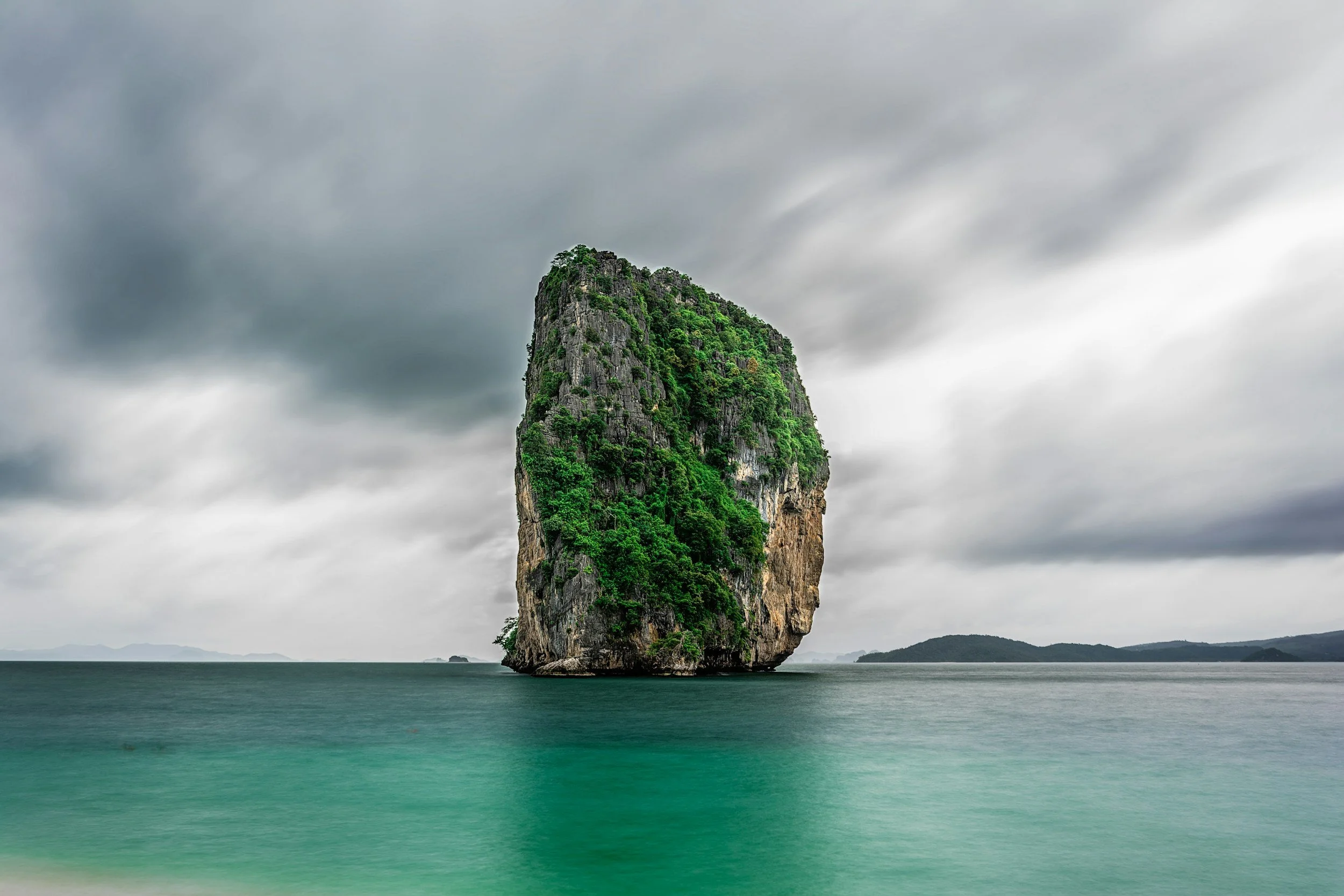 Large limestone island with lush greenery located in a calm sea under a cloudy sky.