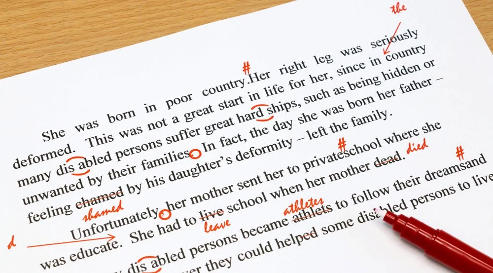 A printed page with handwritten red annotations and corrections, including words such as 'the', 'shamed', 'died', 'leave', and 'athletes', with a red marker pen placed on the paper.