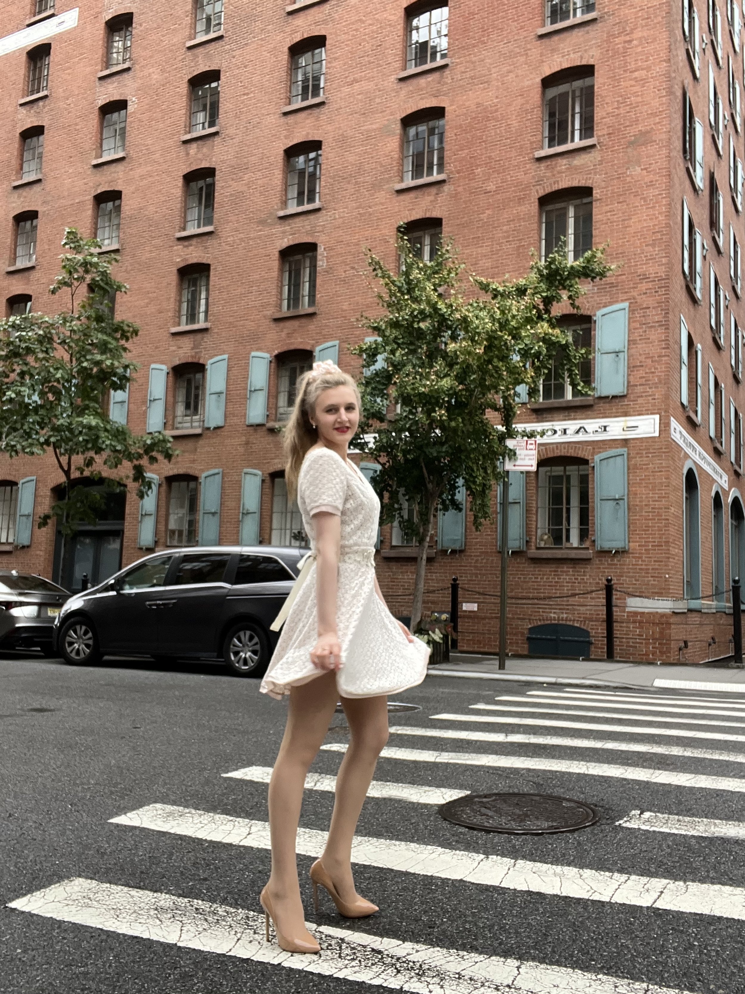 Jacqui de Jong wears a cream lace dress with a white floral belt and nude shoes. 