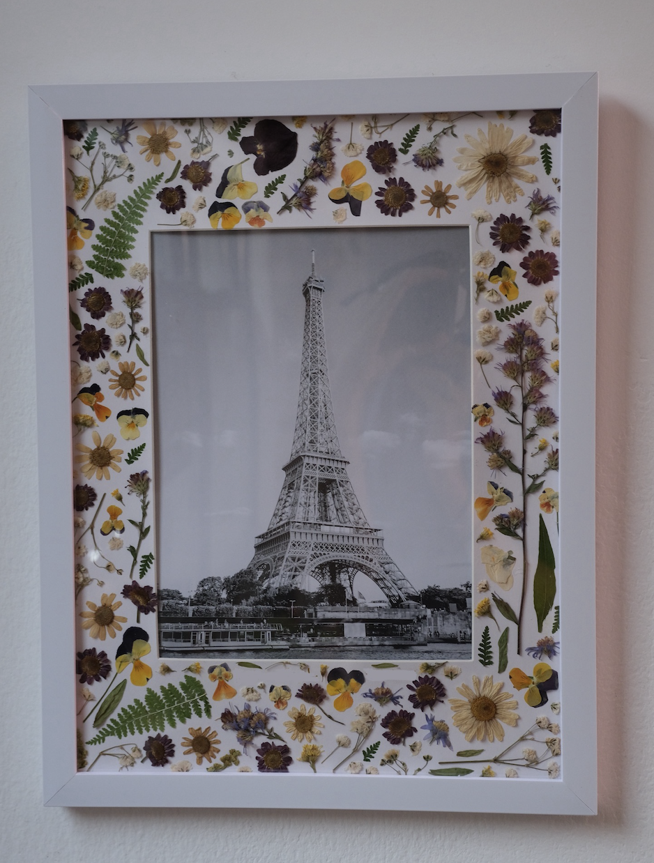 Framed black and white photo of the Eiffel Tower surrounded by a border decorated with pressed dried flowers and small butterfly embellishments.